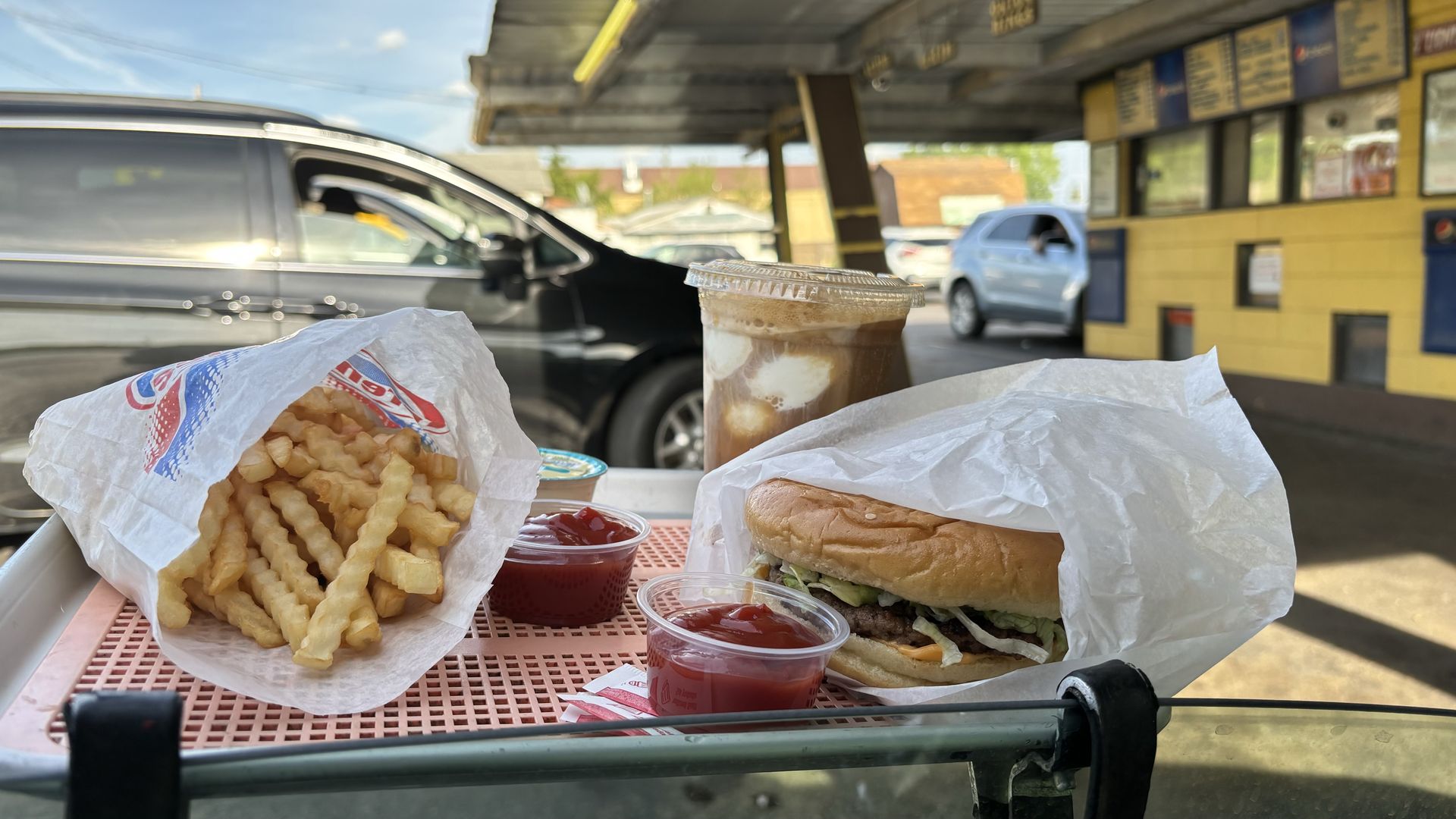 A burger, fries and float on a tray on a car window.