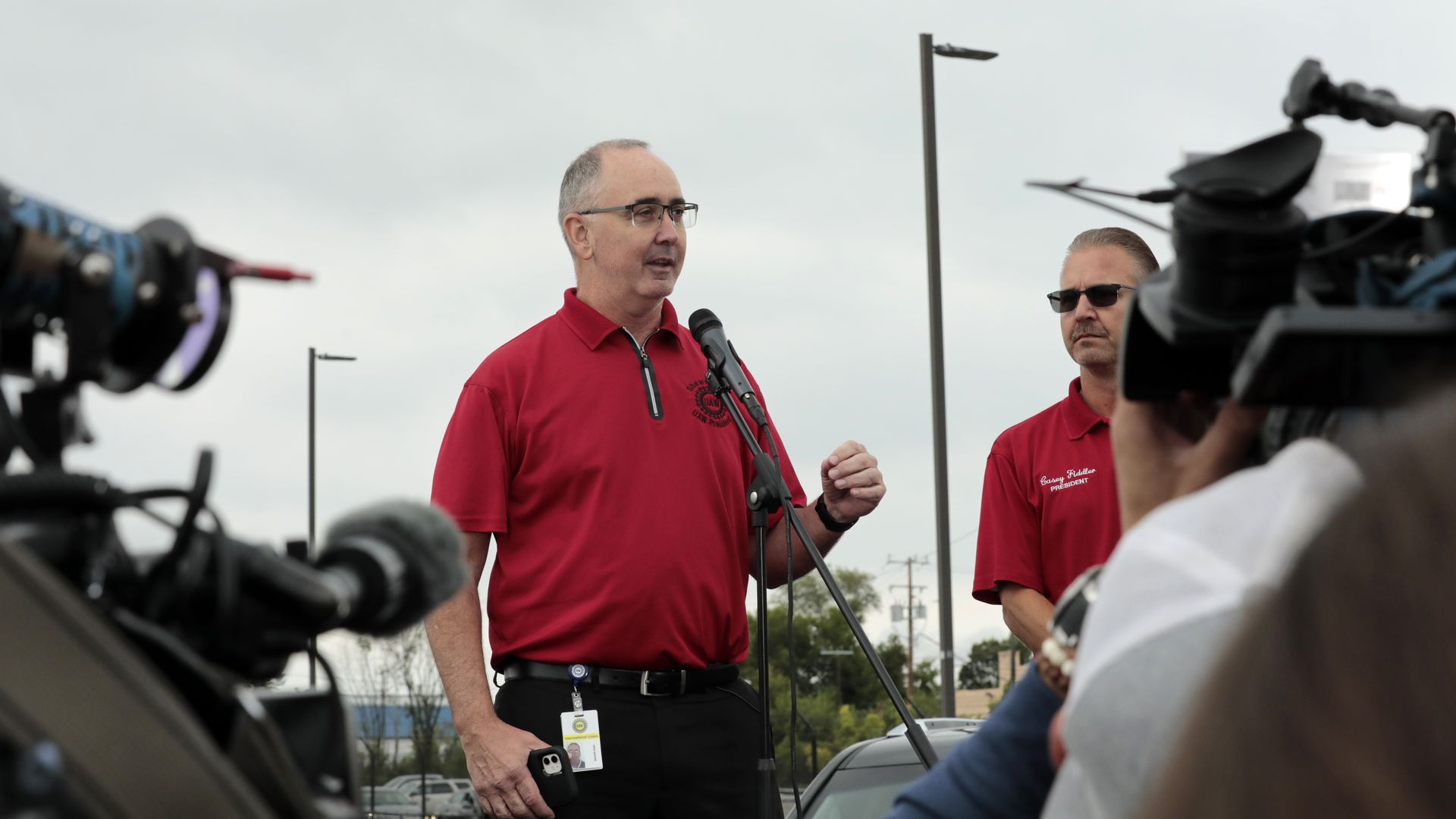 A man in a red shirt address the news media