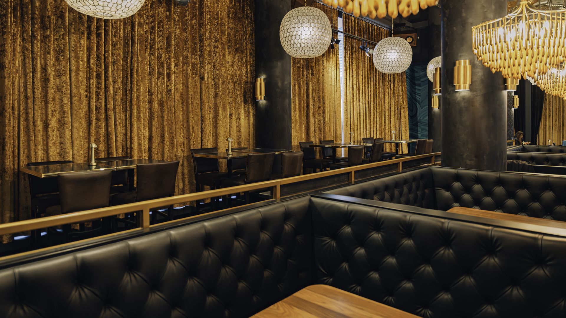 The interior of Grace by Nia, a supper club/speakeasy/live music venue in the Seaport. There are large leather booths and chairs, chandeliers, gilded light fixtures and curtains.
