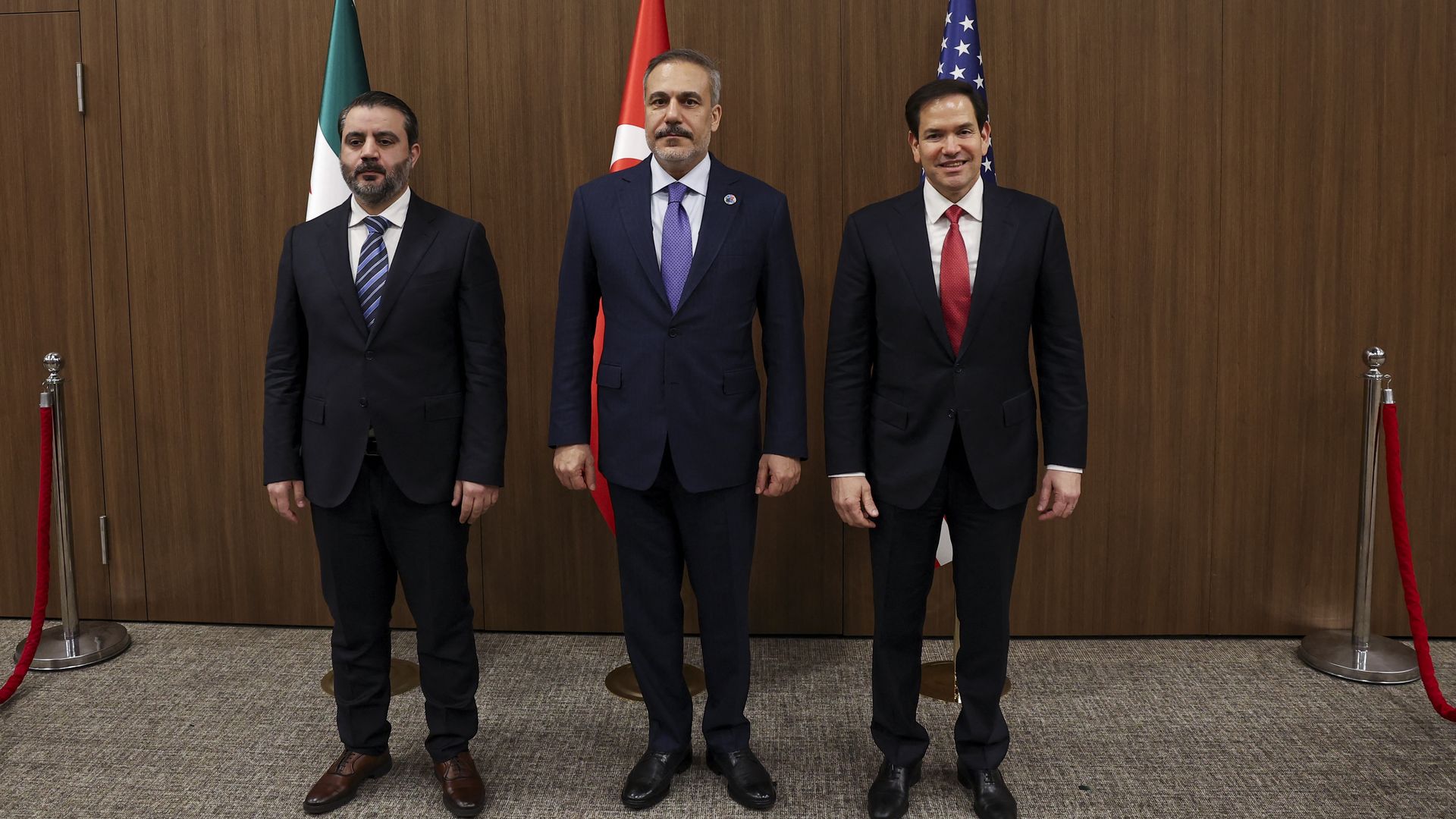Three men in front of flags