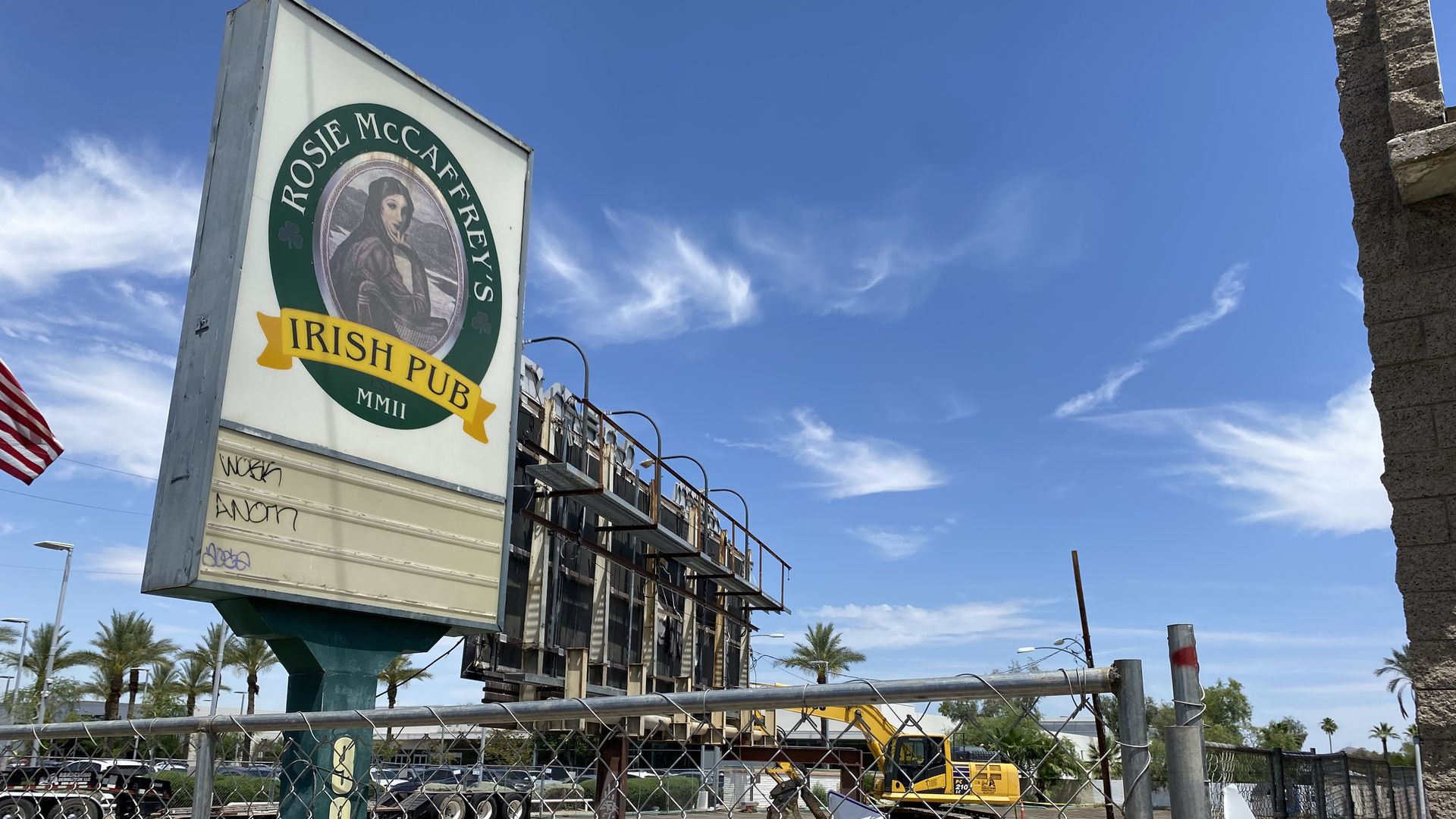 A billboard, excavator and sign advertising an Irish pub sit on an otherwise vacant lot.