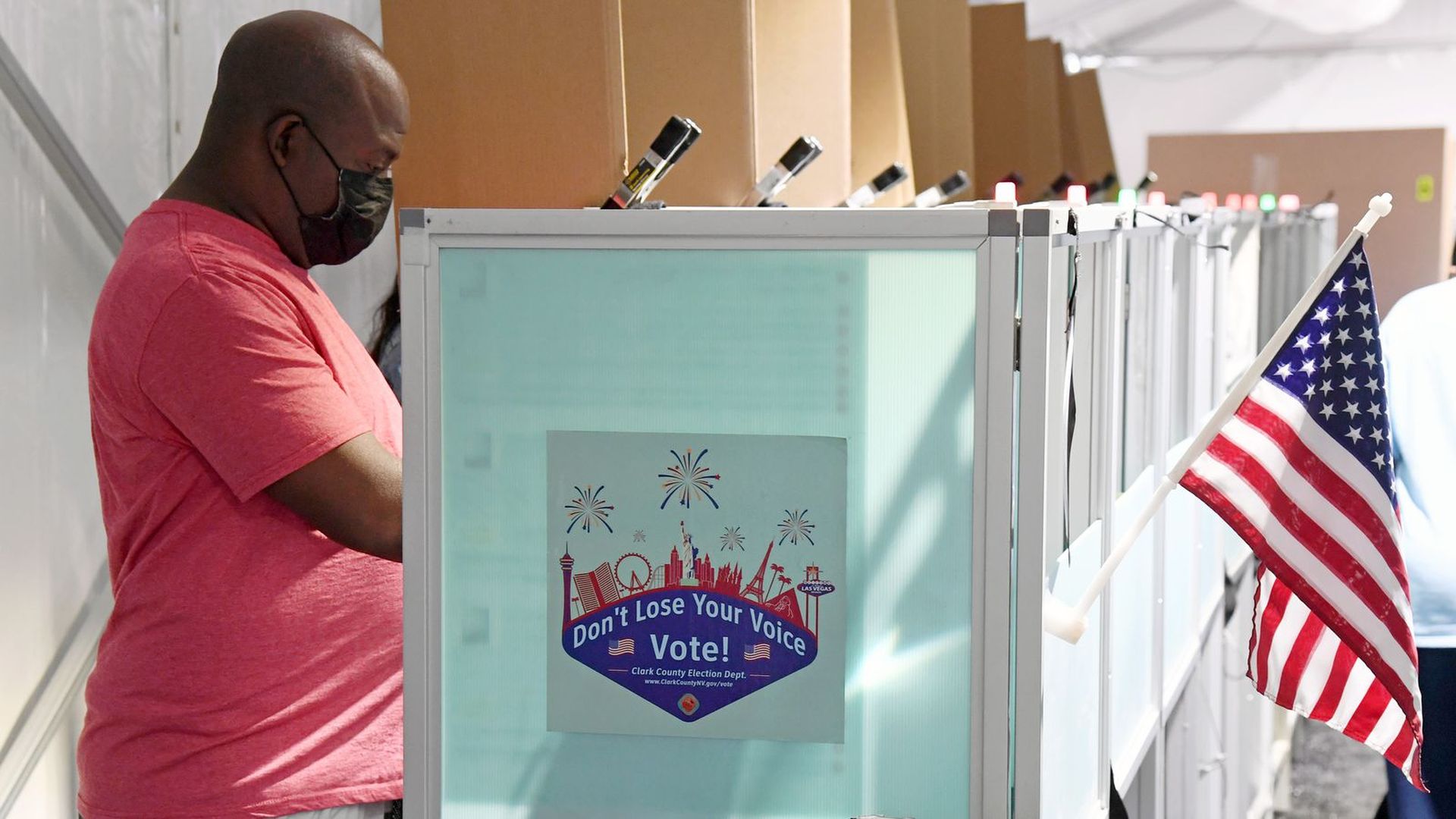 A voter in a coral shirt wearing a mask casts his vote in the 2020 election.