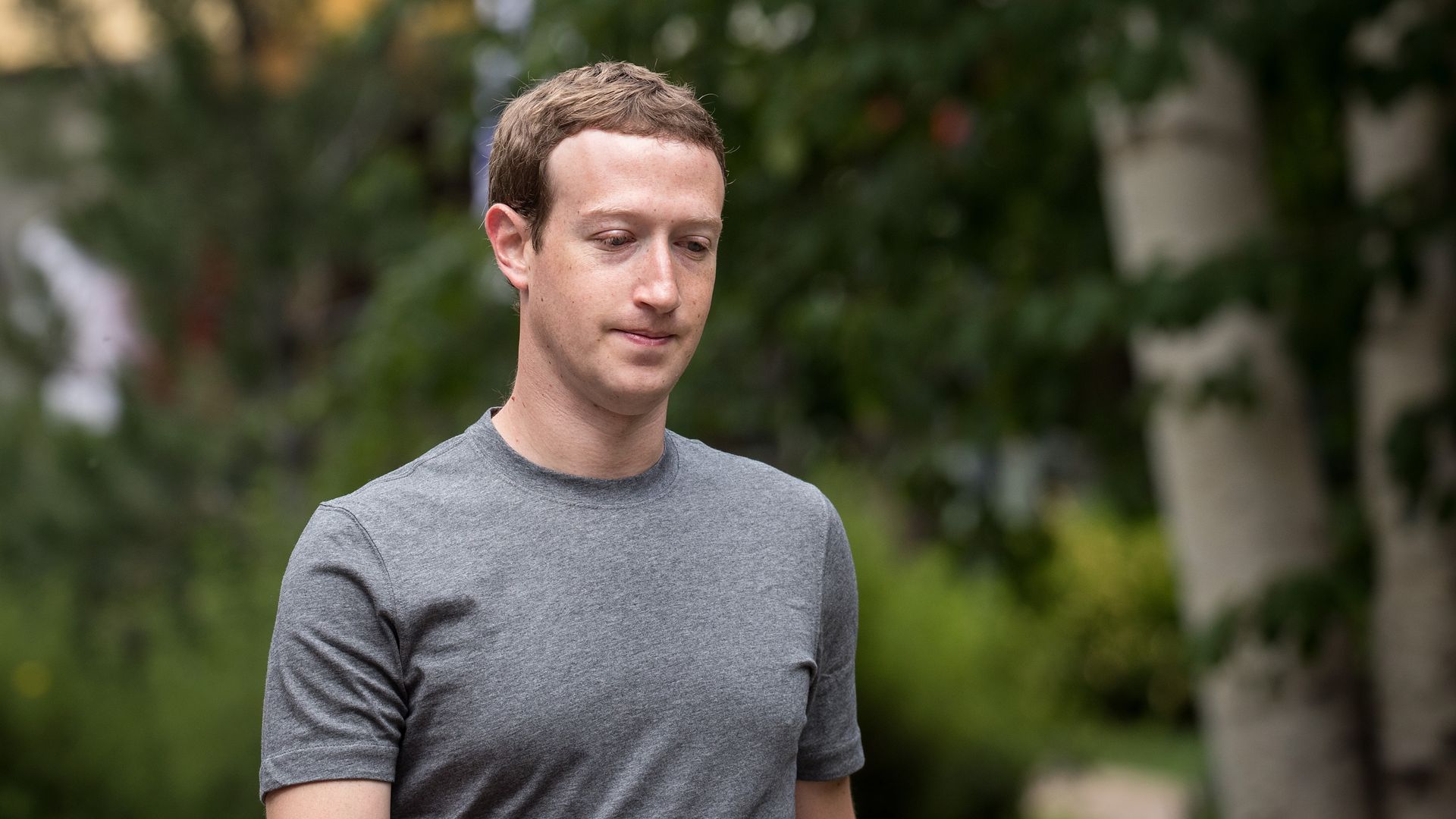 Facebook CEO Mark Zuckerberg walks wearing a t-shirt, with trees behind him