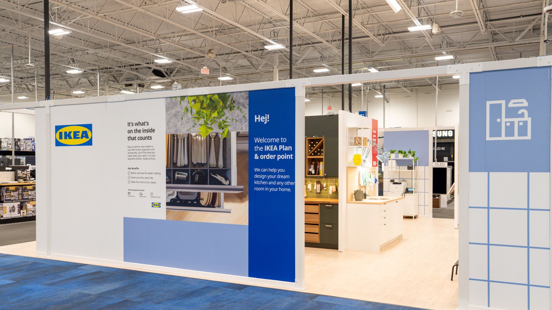 IKEA showroom section with blue and white walls, sign welcoming visitors to IKEA Plan & order point, and displays of kitchen setups set up in a Best Buy store. 