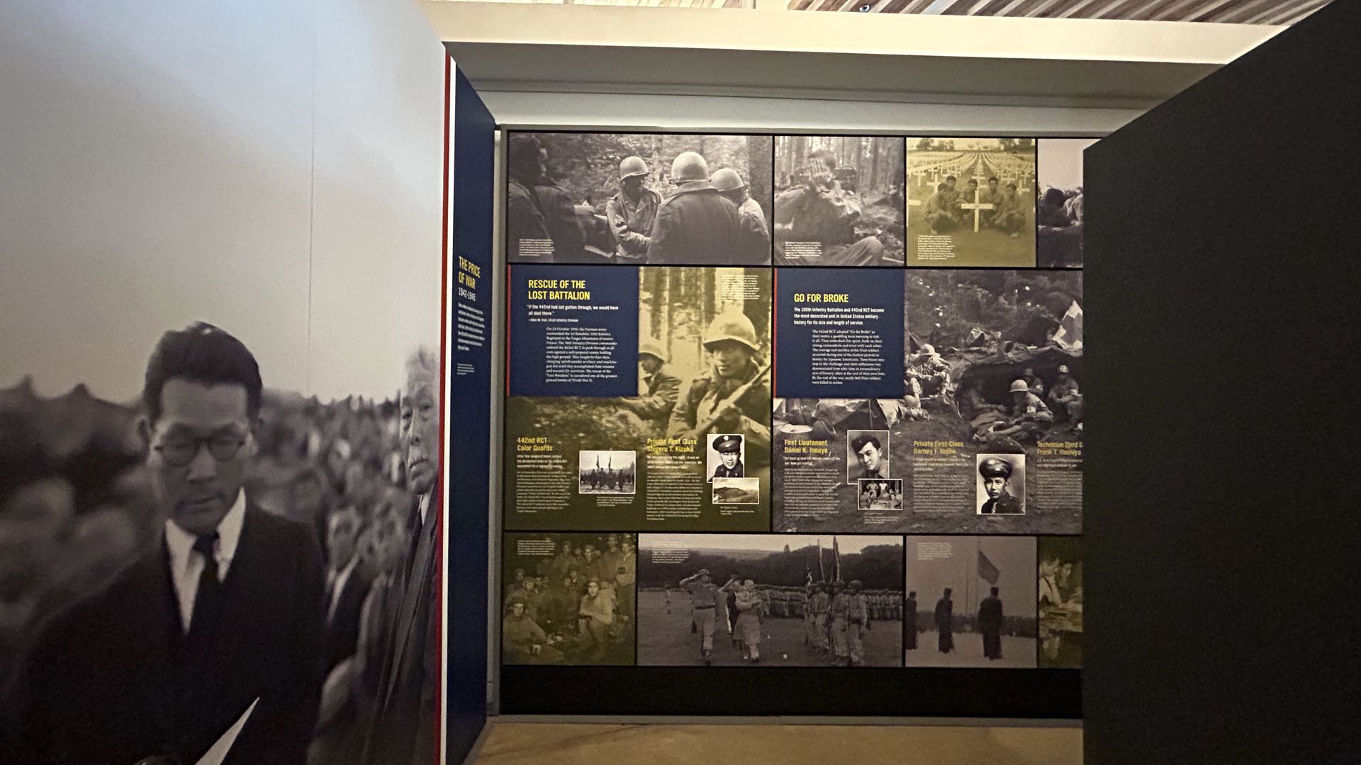 Museum exhibit with black and white wartime photos and text panels about the 442nd Infantry Battalion and the Rescue of the Lost Battalion, featuring soldiers and memorial scenes.