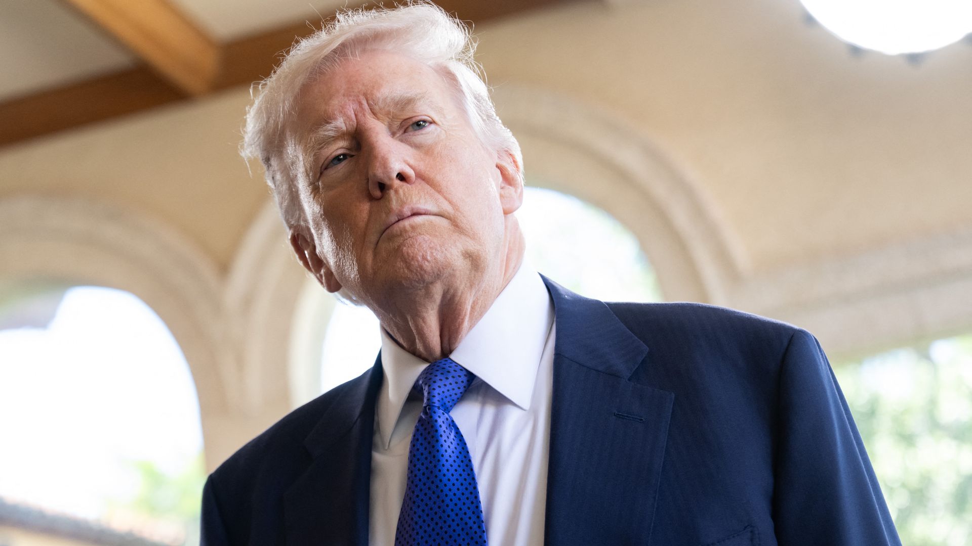 President Trump, in a suit and white shirt with blue tie, standing outside and looking toward reporters. 