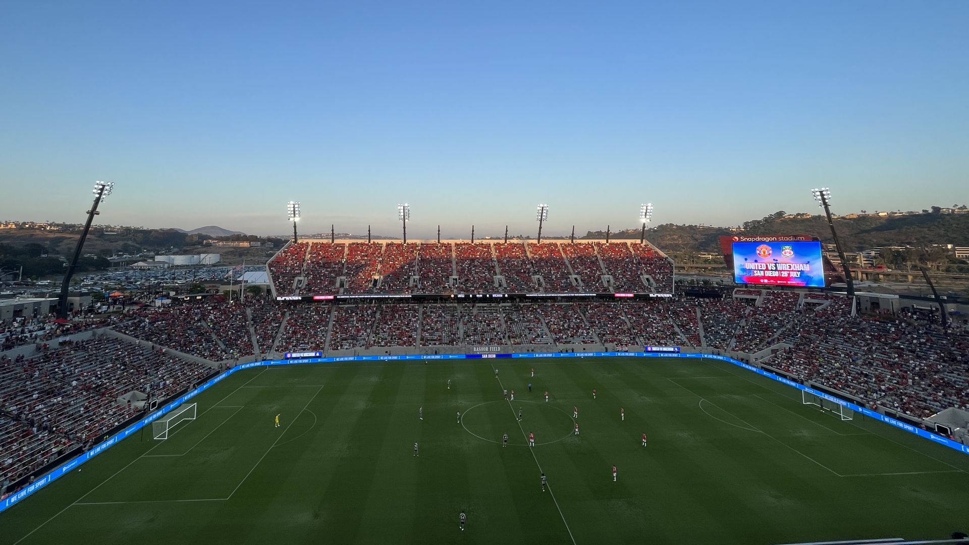 Professional soccer players line up in starting positions on a field at a stadium filled with fans at dusk.