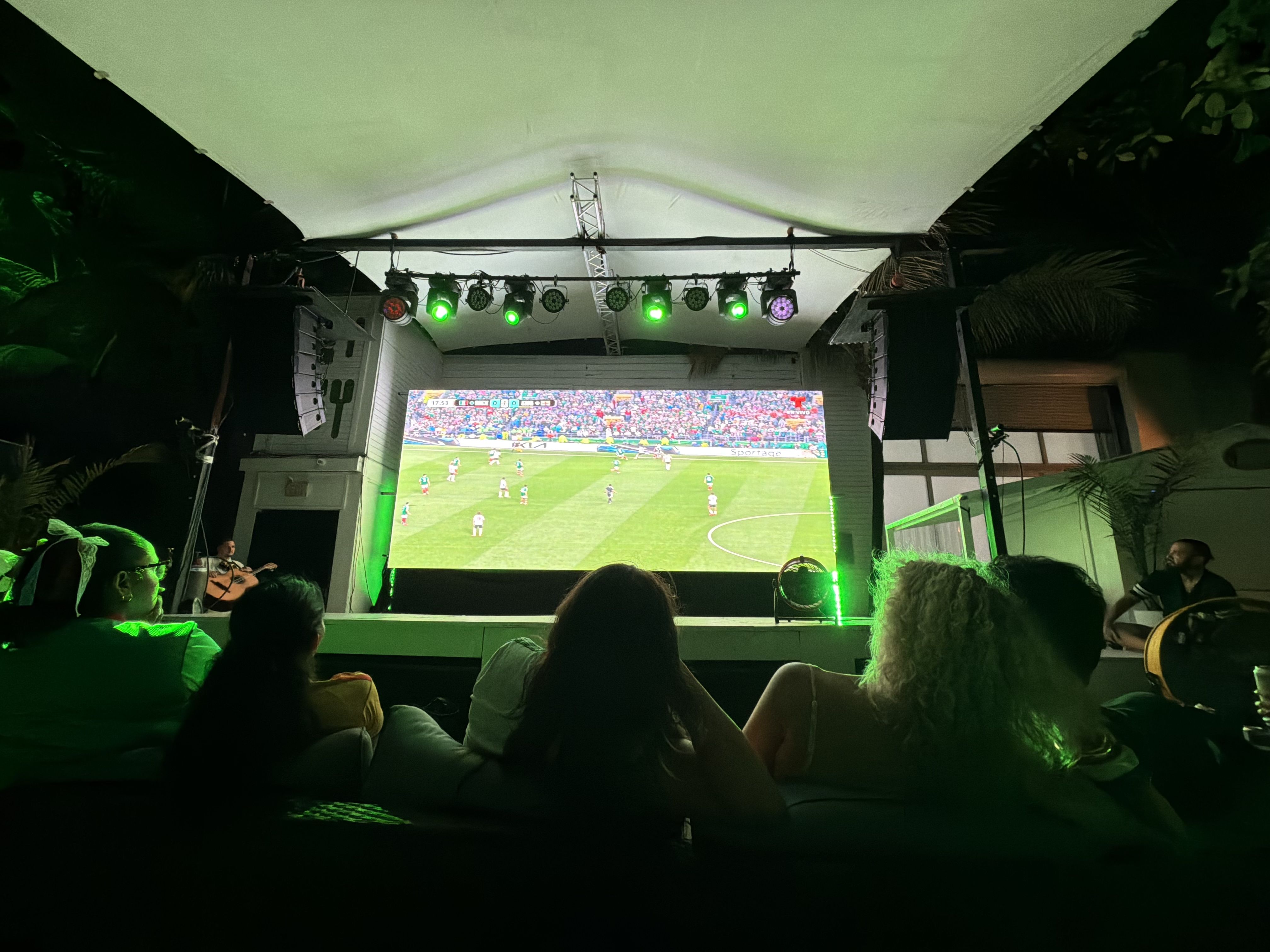 Nighttime outdoor viewing area with a large soccer match on a bright screen. 