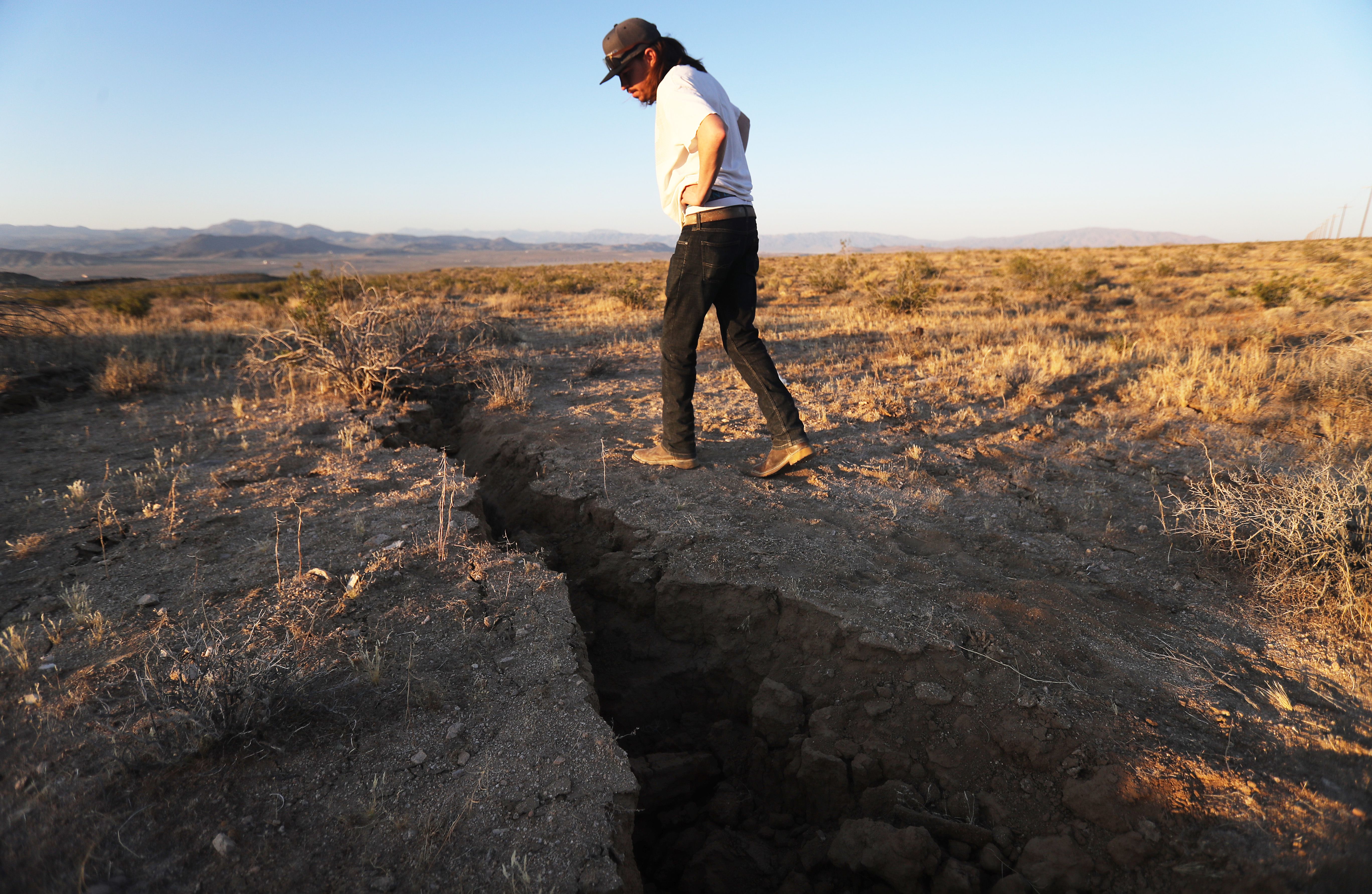 This image shows a man inspecting a fissure in the ground in the desert.
