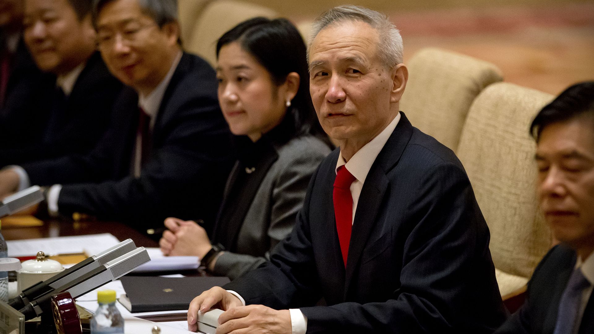 In this image, Vice Premier Liu He sits at a conference table in a beige chair next to other professionally dressed men and women.