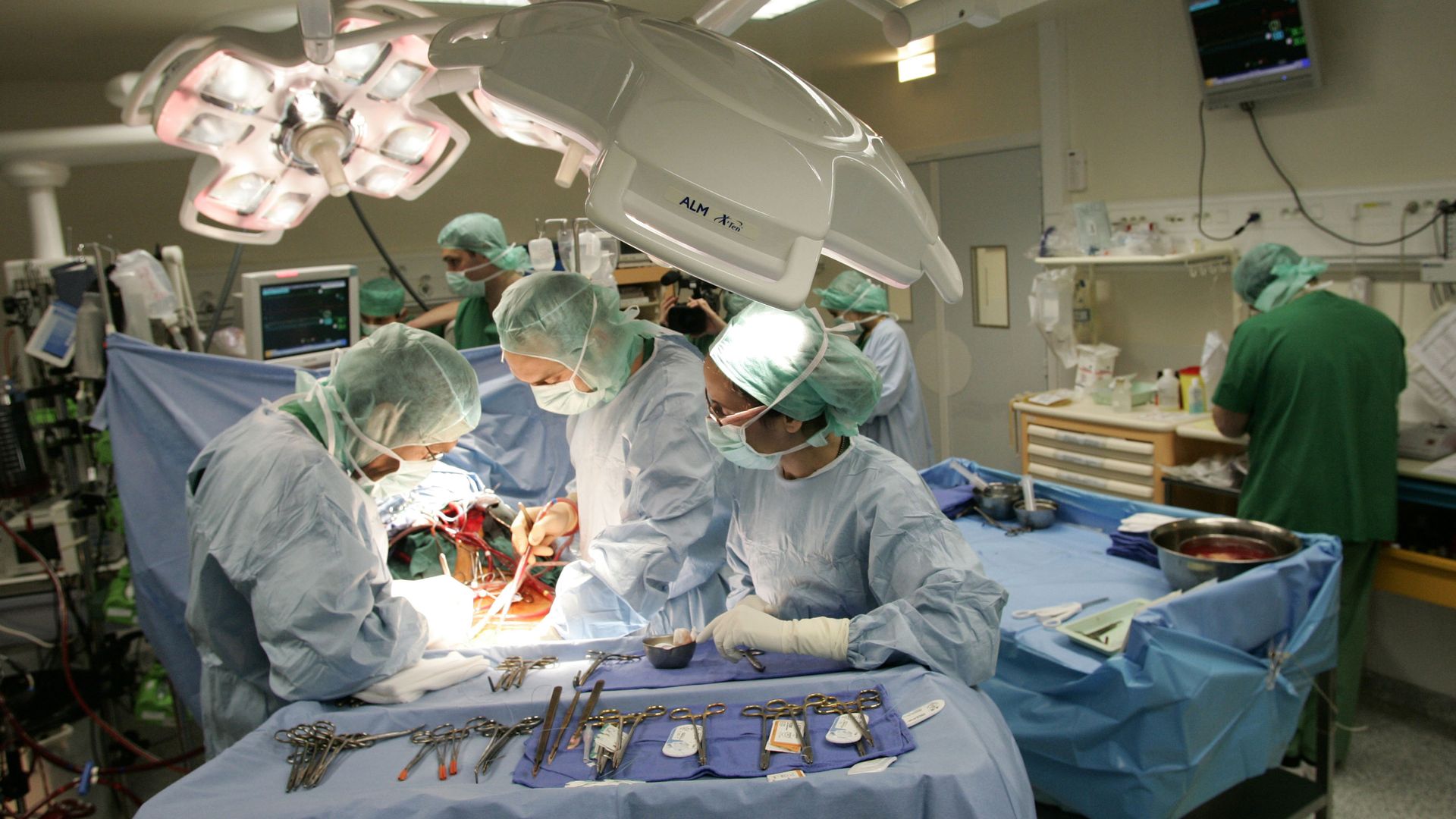 Three doctors in gowns surround a patient on an operating table.