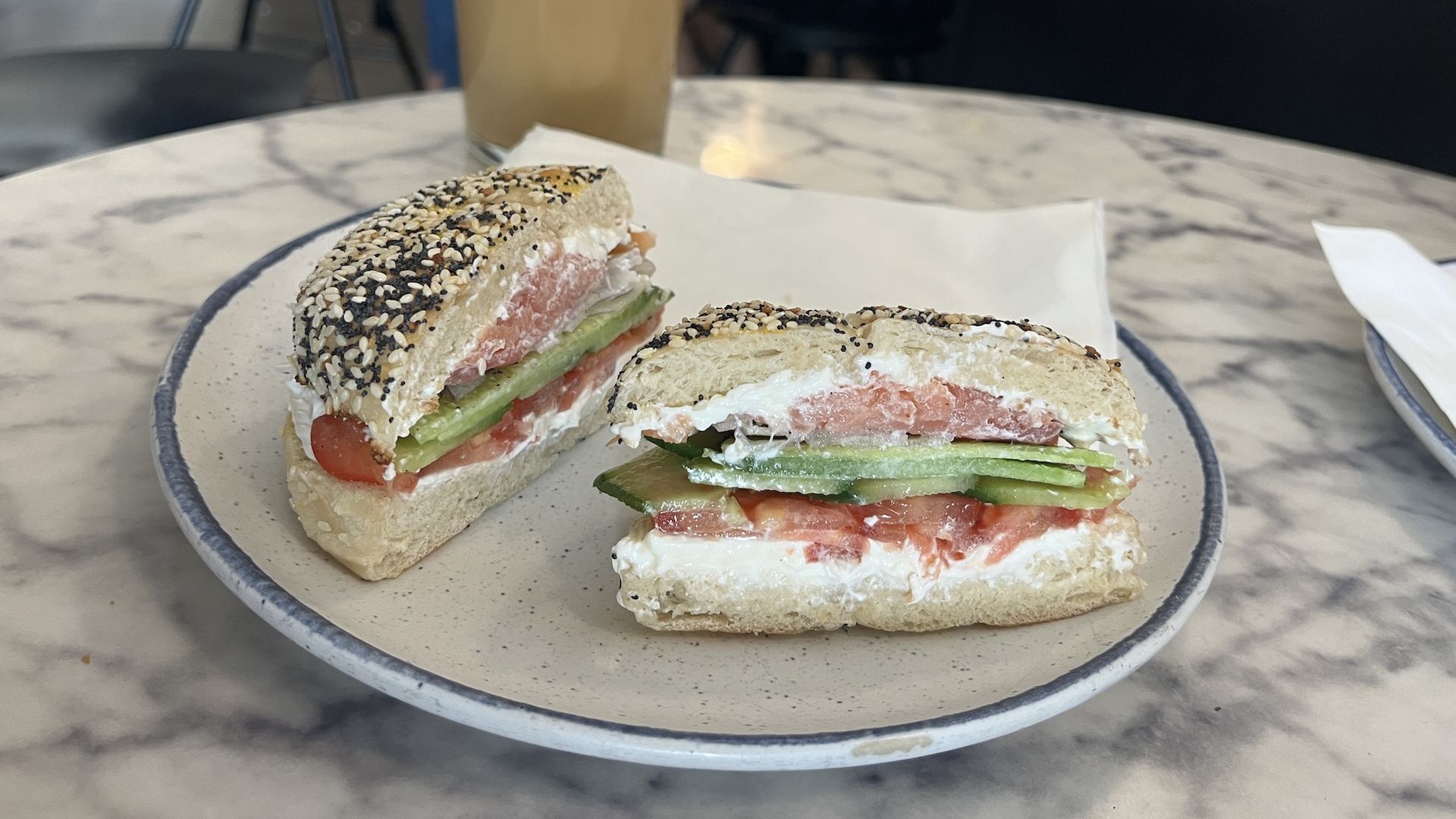 An everything bagel sandwich with lox, cream cheese, sliced cucumber, tomato, and red onion.