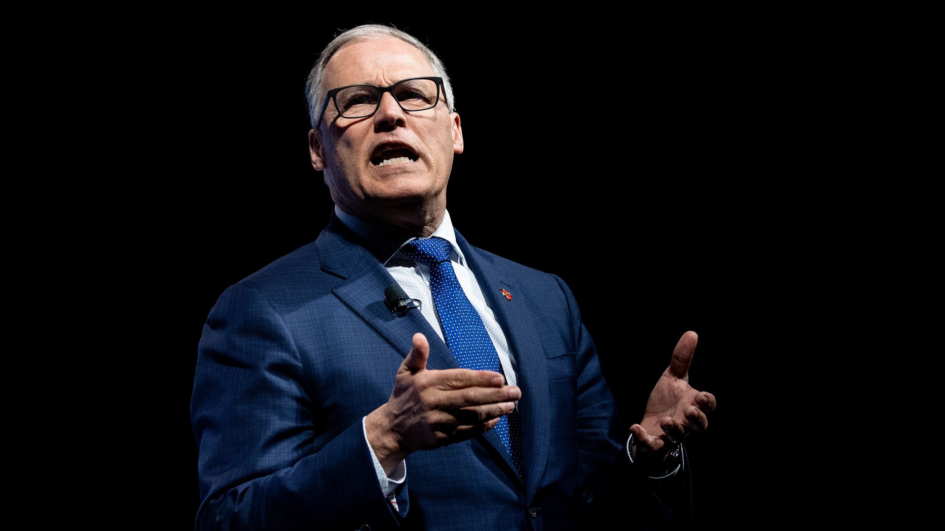 In this image, Jay Inslee speaks in a suit and tie while gesturing both hands.