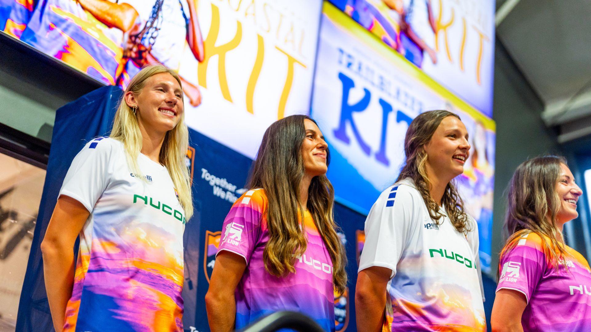 4 female soccer players standing in front of signs. 
