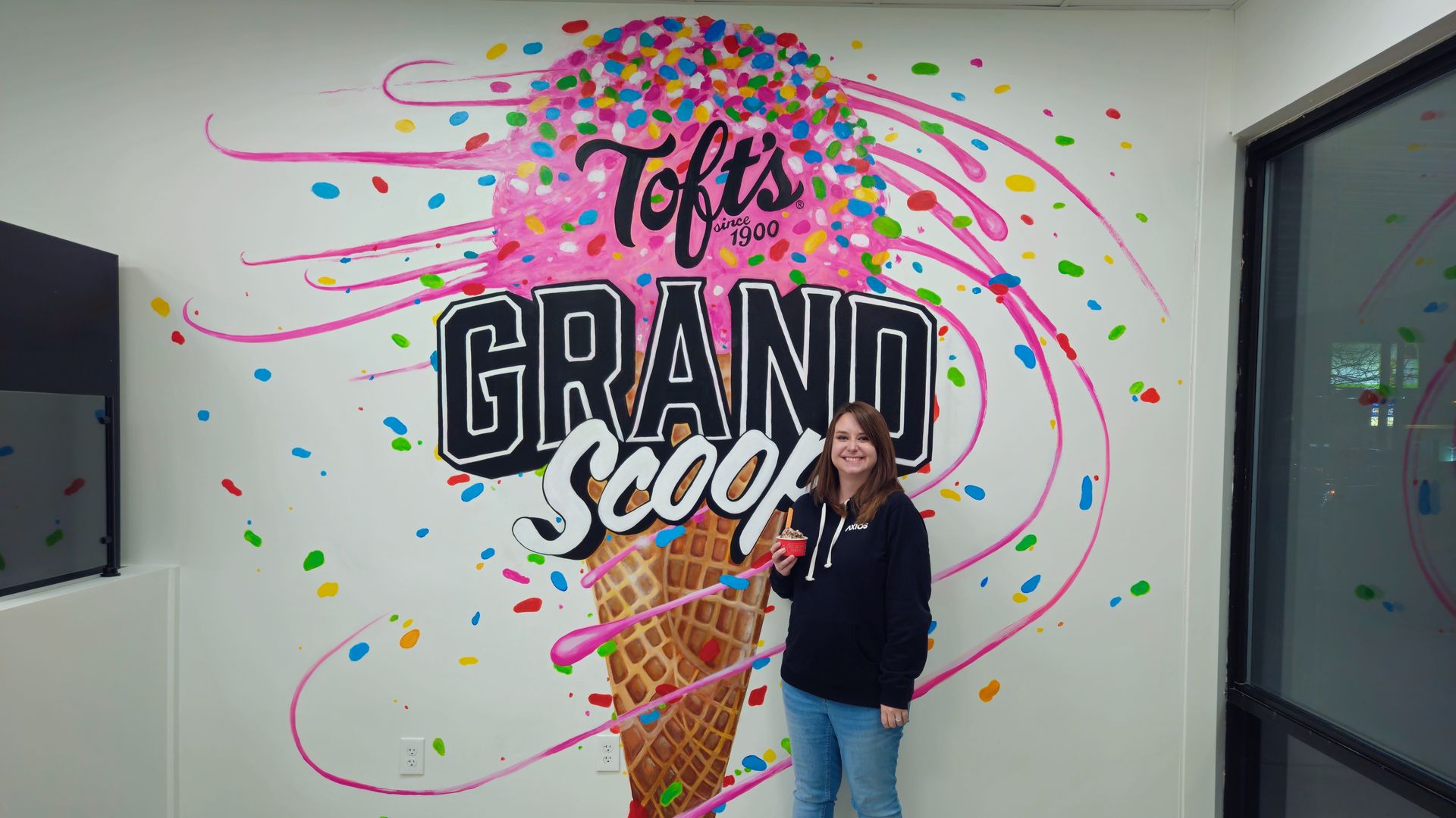 Alissa stands in front of a wall that reads "Toft's Grand Scoop" with a pink ice cream cone painting
