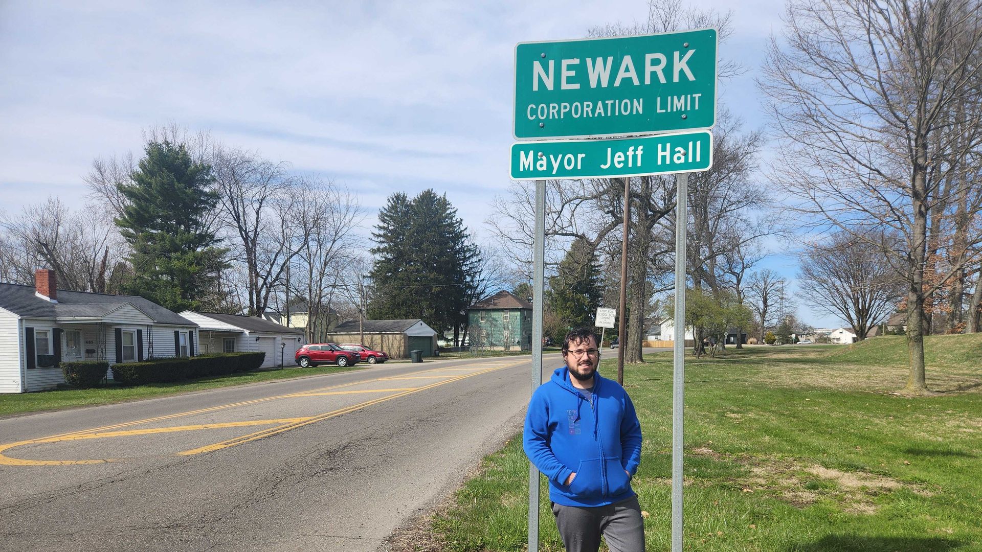 Tyler standing in front of a Newark corporation limit sign on the side of a road.