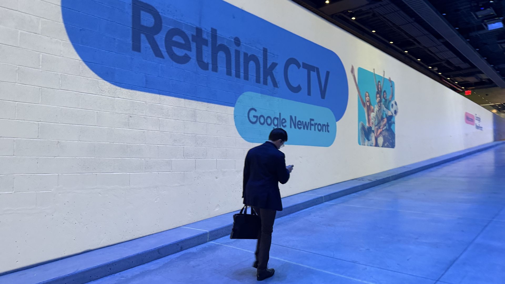 A person in a suit is looking at his phone, holding a brief case and walking up a ramp. Next to him is a screen that says Rethink CTV Google NewFront