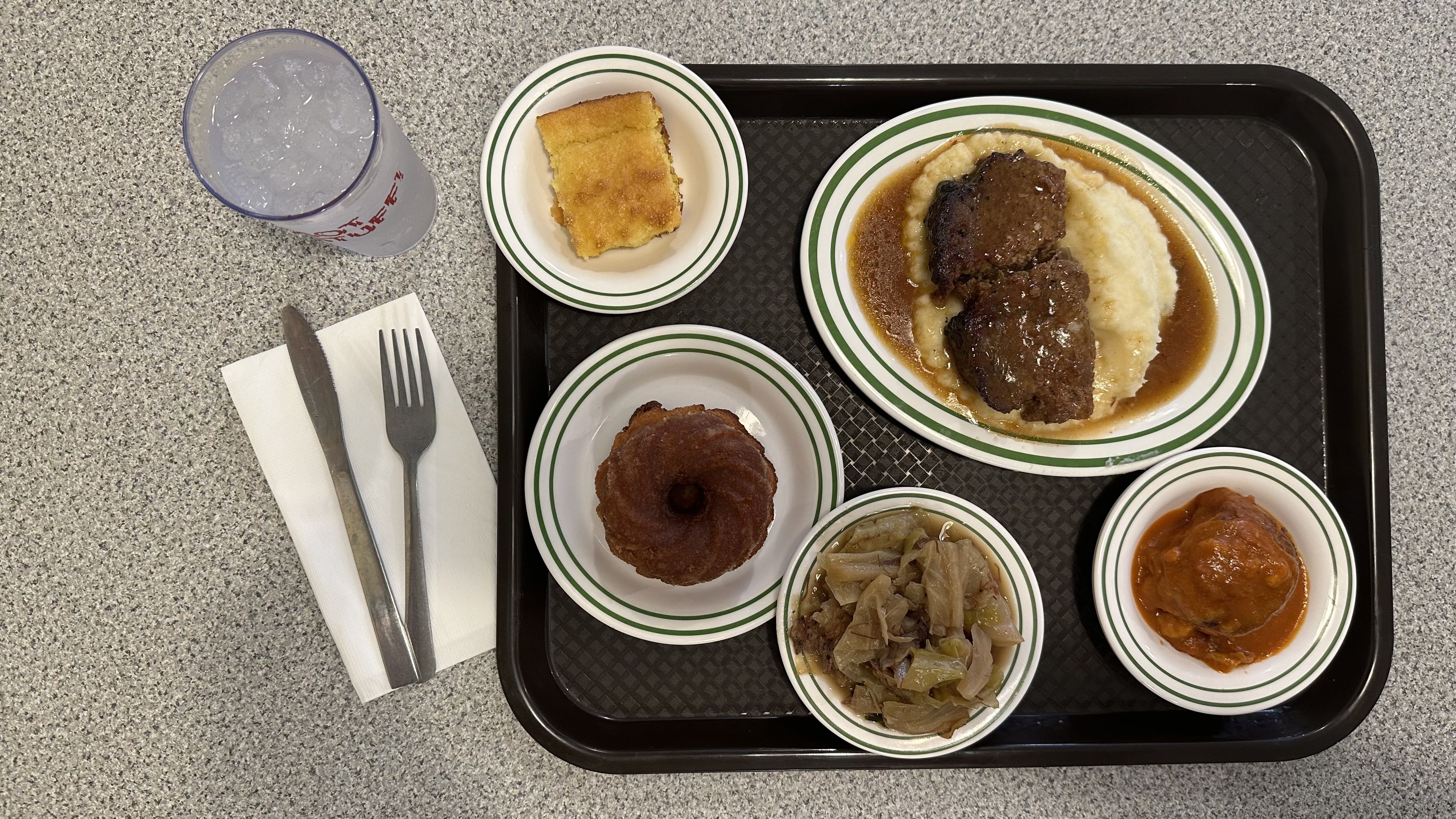 A lunch tray, viewed from above, with meatloaf and several sides.