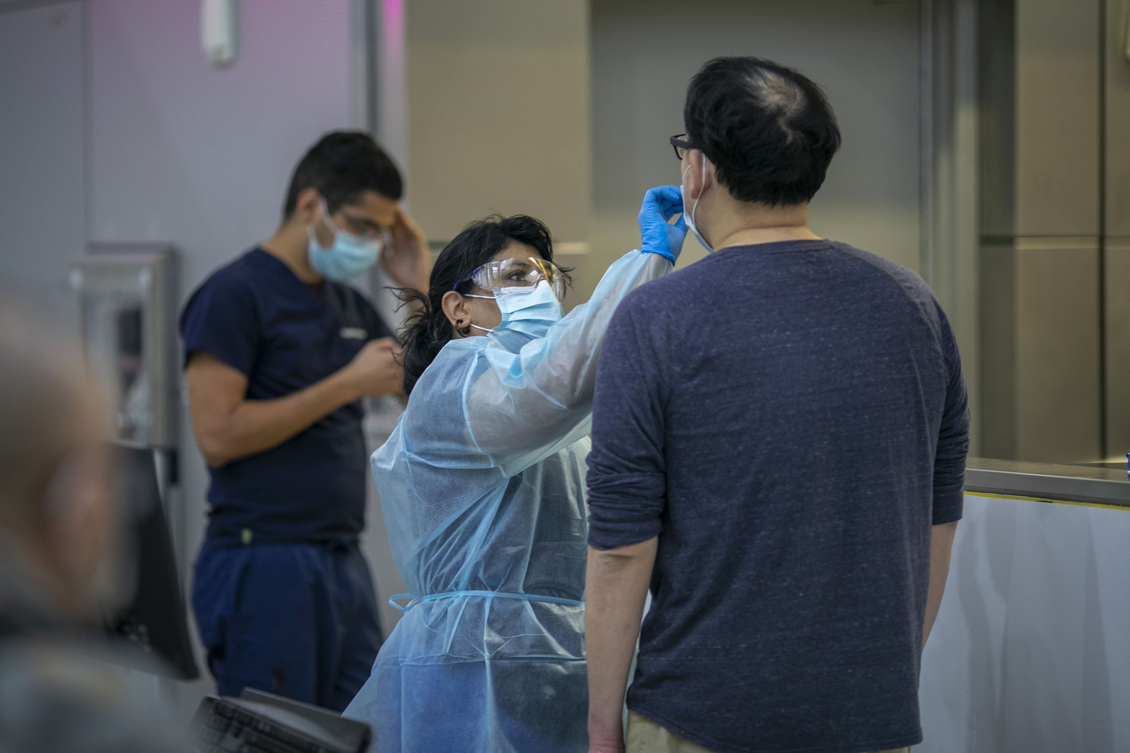 A man wearing a T -shirt is tested for COVID by a woman wearing a face mask and PPE 