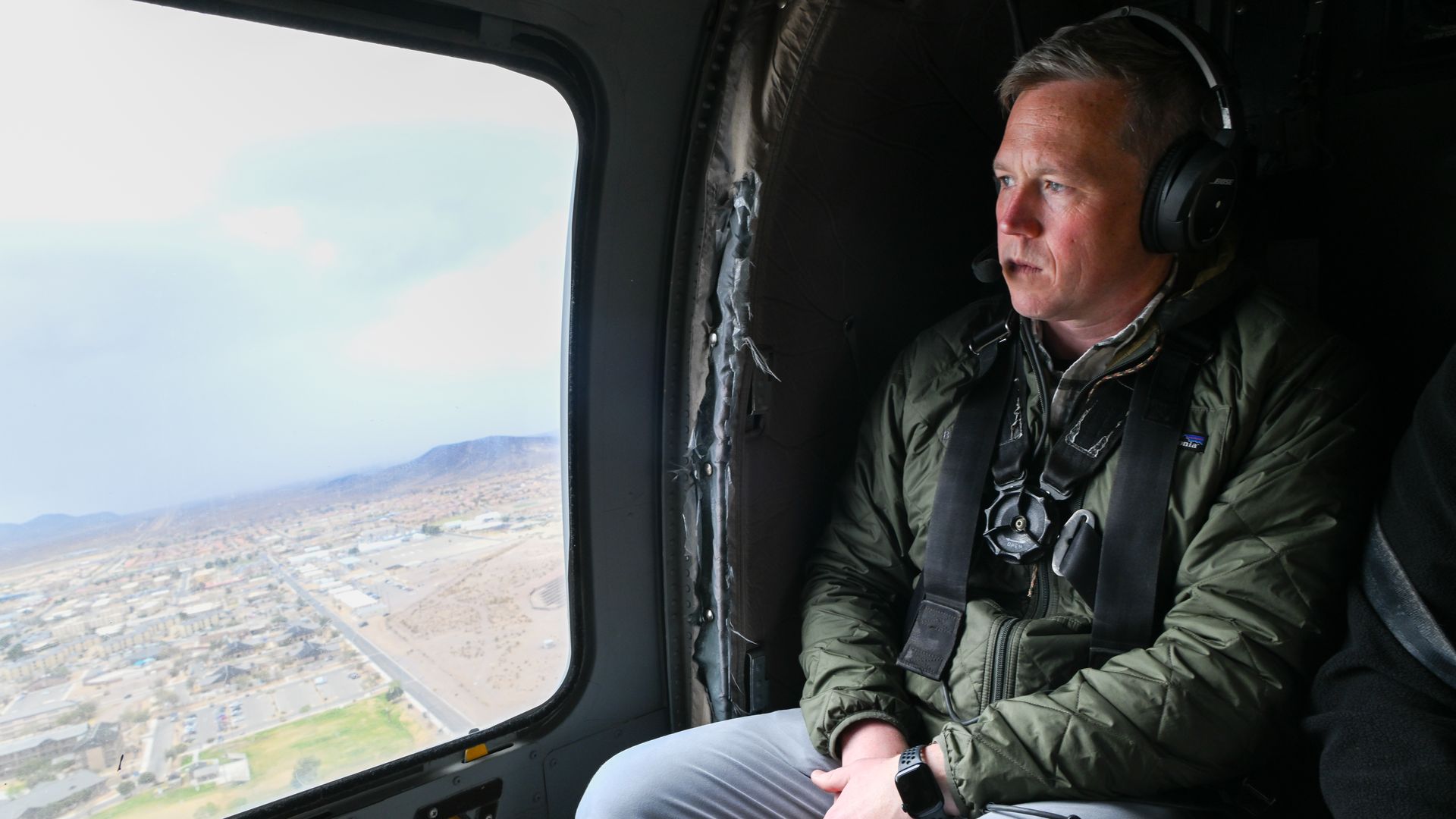 Dan Driscoll, a man, is seated in a Black Hawk helicopter and looking out the window at the ground below.