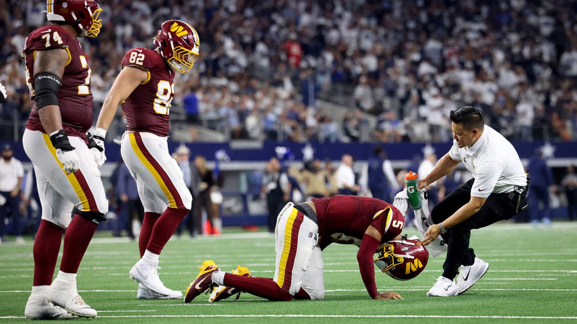 Washington Commanders quarterback Jayden Daniels falls to the ground after being injured while his teammates stand over him.