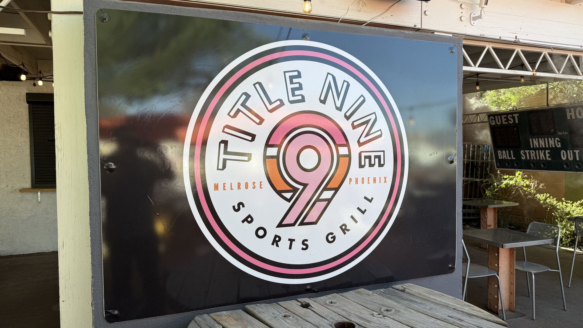 A sign atop an outdoor table at a bar patio with a circular logo for Title Nine Sports Grill. 