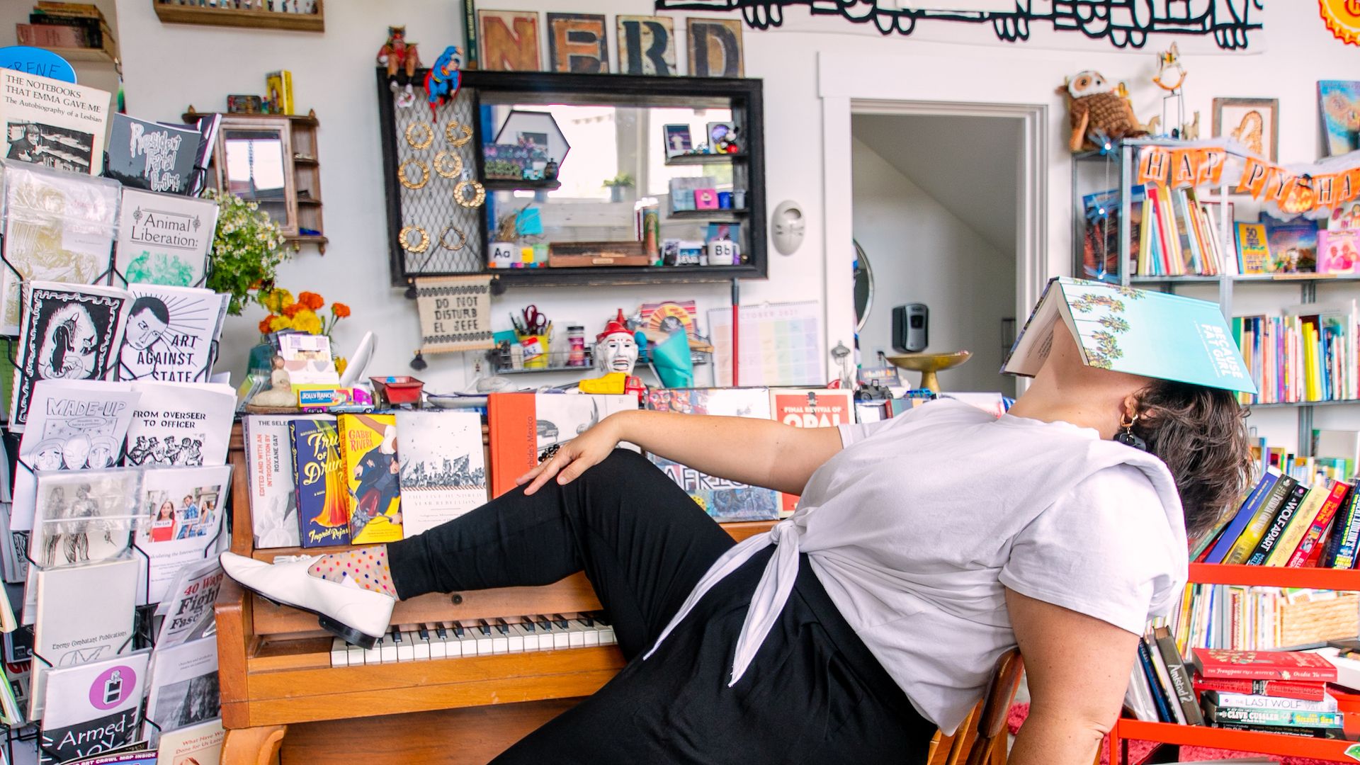 A woman sitting at a piano asleep with a book over her face. 