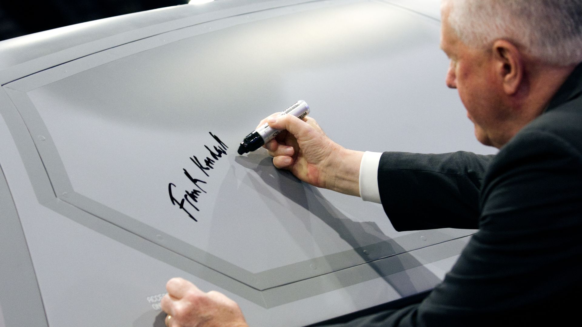 Frank Kendall, a man, signs a drone with a very thick, black Sharpie.