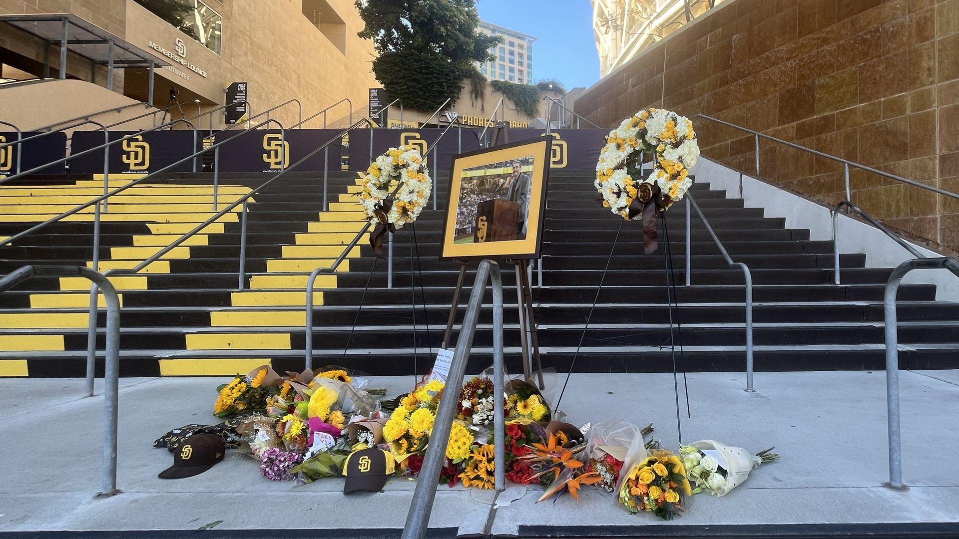 A memorial with a framed photo on an easel, bouquets of flowers and San Diego Padres hats. 