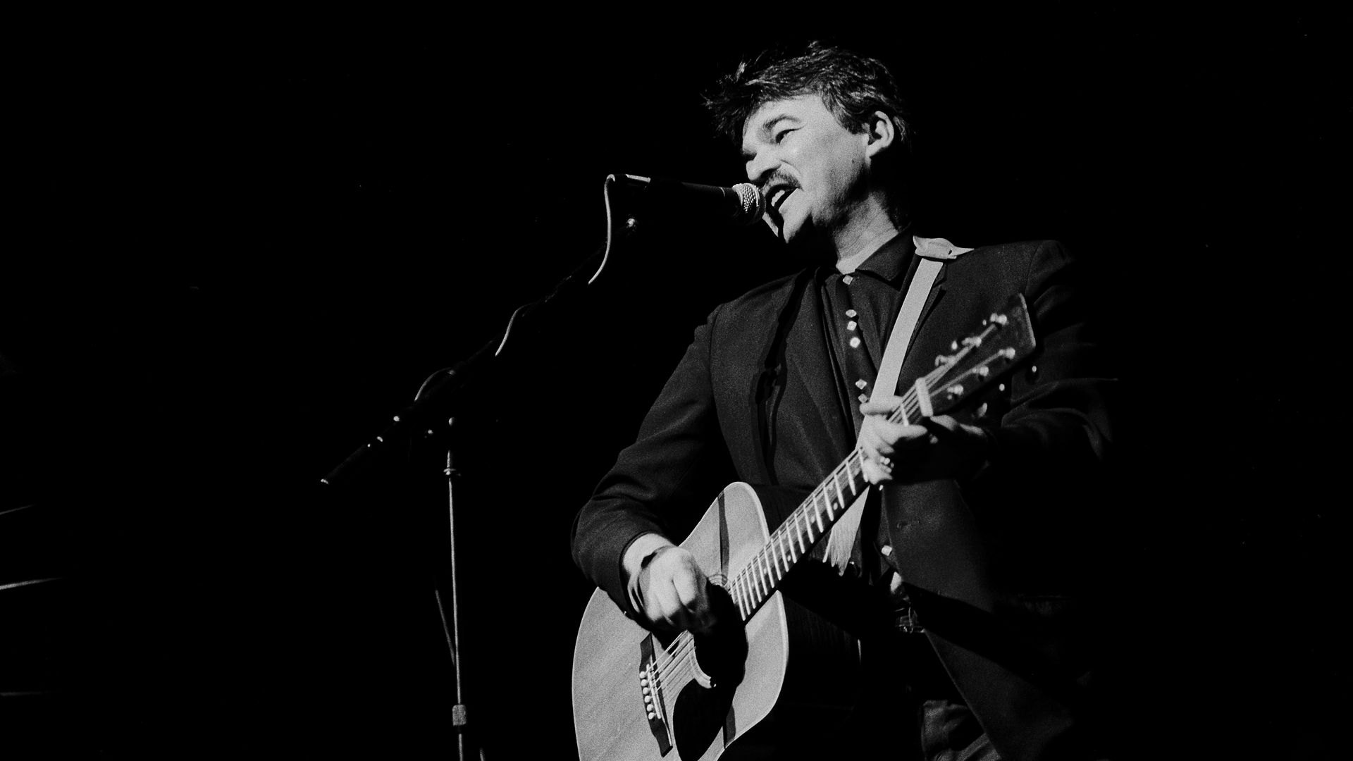 black and white photo of a man with a guitar on stage