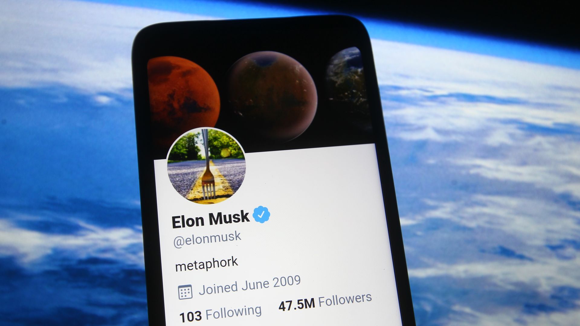 In this photo illustration a Twitter webpage of Elon Musk is seen on a smartphone screen in front of Spacex website..