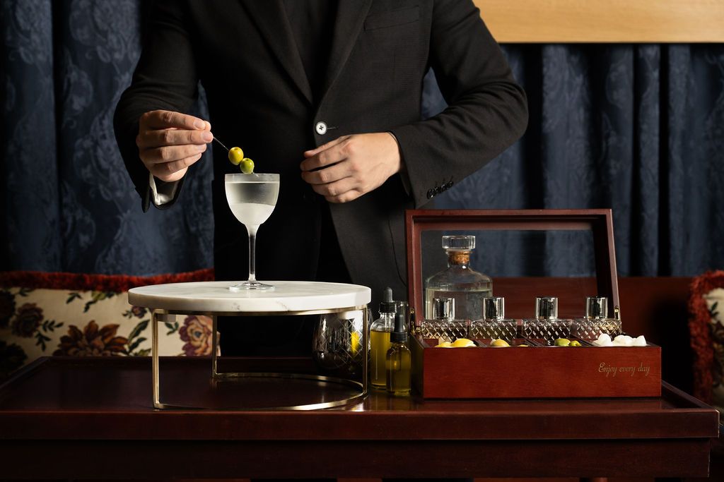 A person placing olives into a martini on an elaborate bar setup