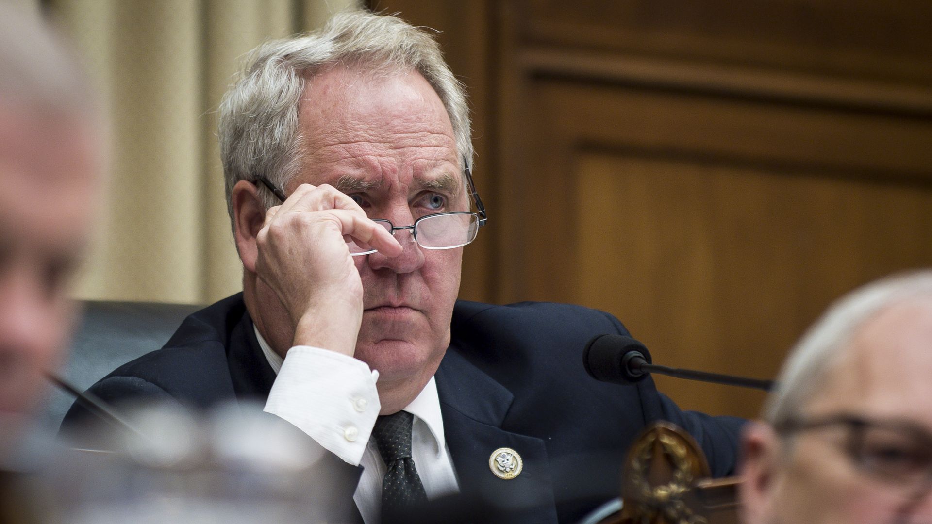 In this image, Shimkus adjusts his glasses while at a hearing. He's wearing a suit.