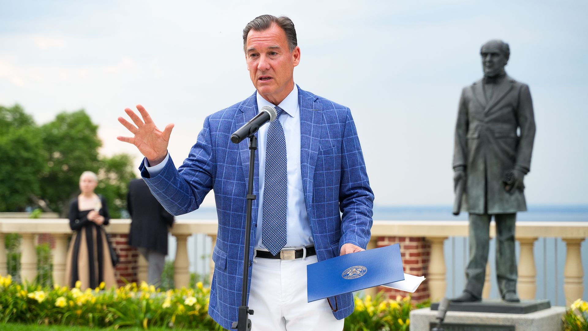 Tom Suozzi, wearing a blue suit and white pants and standing outside.