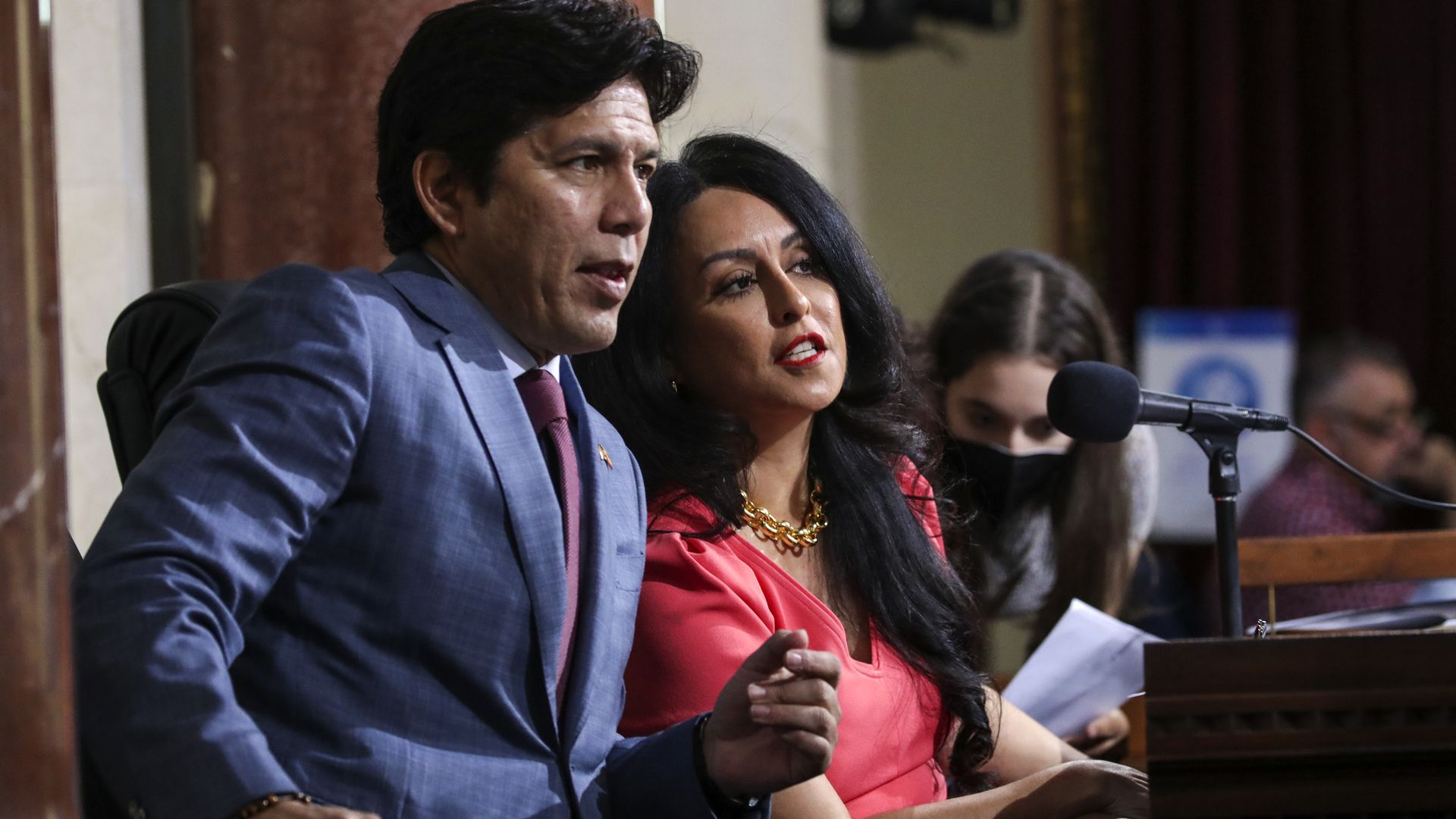 Los Angeles Councilman Kevin de León and Los Angeles City Council President Nury Martinez speak among themselves behind a microphone, both looking off to the side