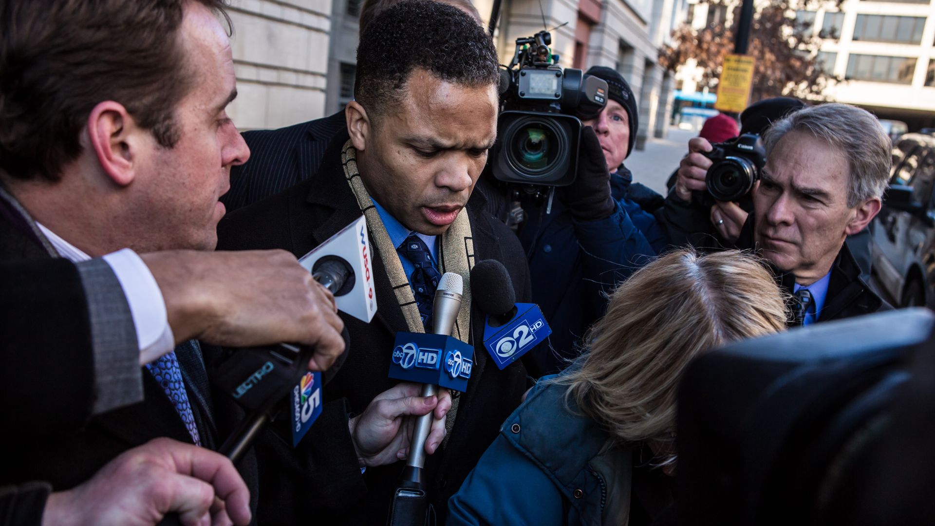 Photo of a man getting asked questions by a number of reporters holding microphones 