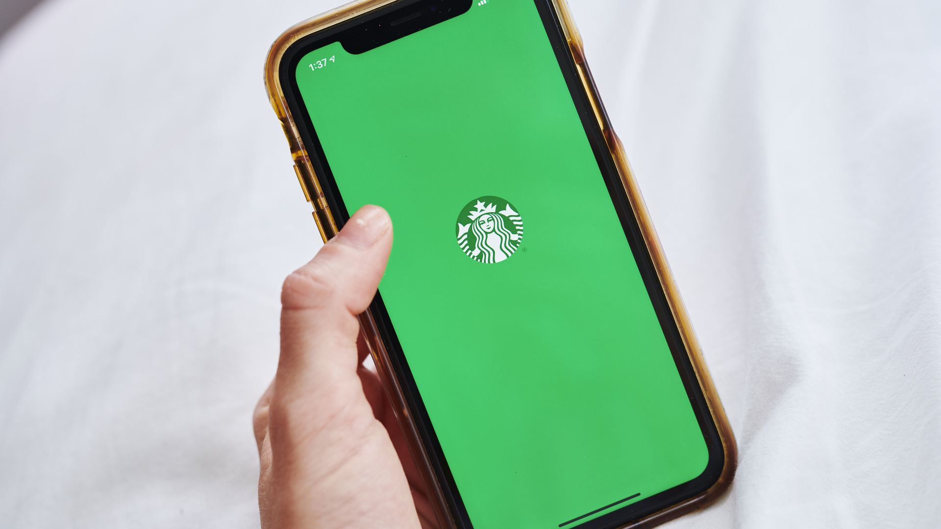 Hand holding phone with green screen and Starbucks siren logo