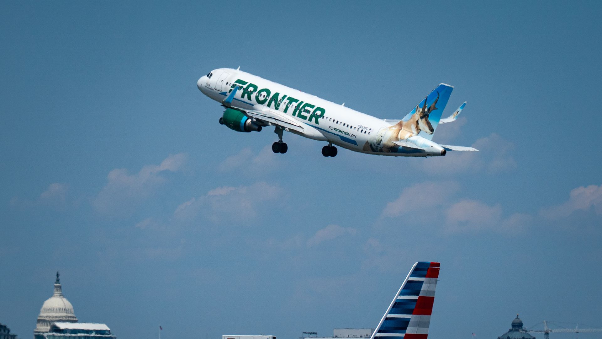 a frontier airlines plane in the air with the US capitol in the background
