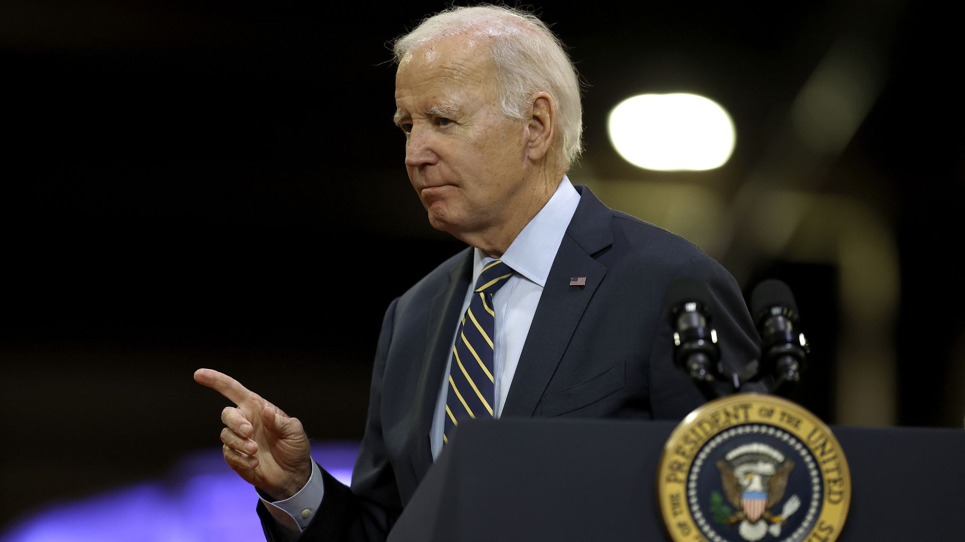 President Biden, standing behind microphones at a podium, points to someone in the crowd during a speech in Delaware.