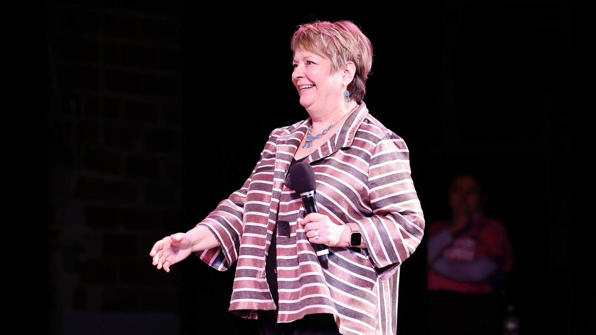 Picture of Janet Protasiewicz wearing a pink and purple striped jacket and holding a microphone