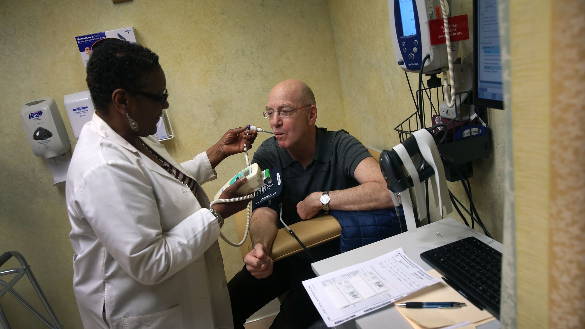 A nurse checks a patient whose medical records sit on a desk.