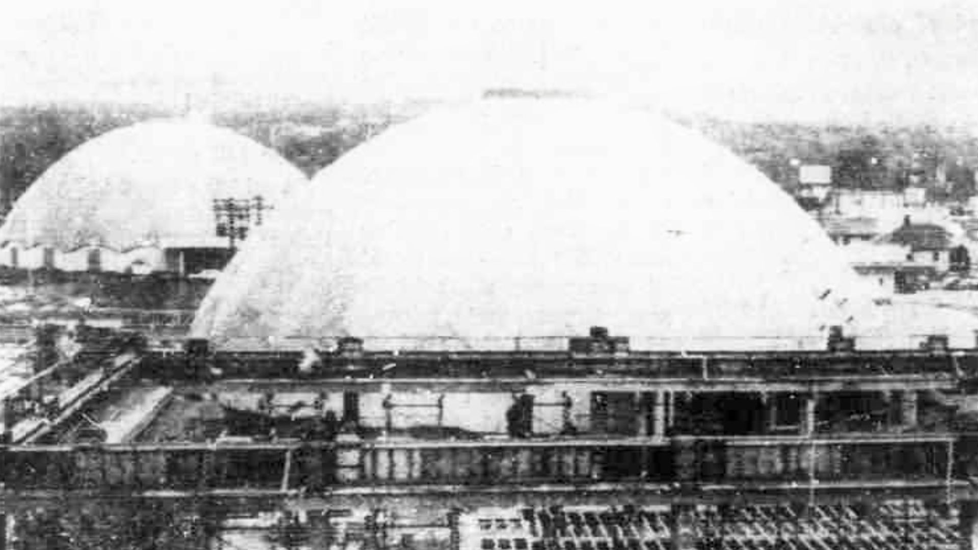 Two domed buildings stand next to each other in a black and white picture of a city.