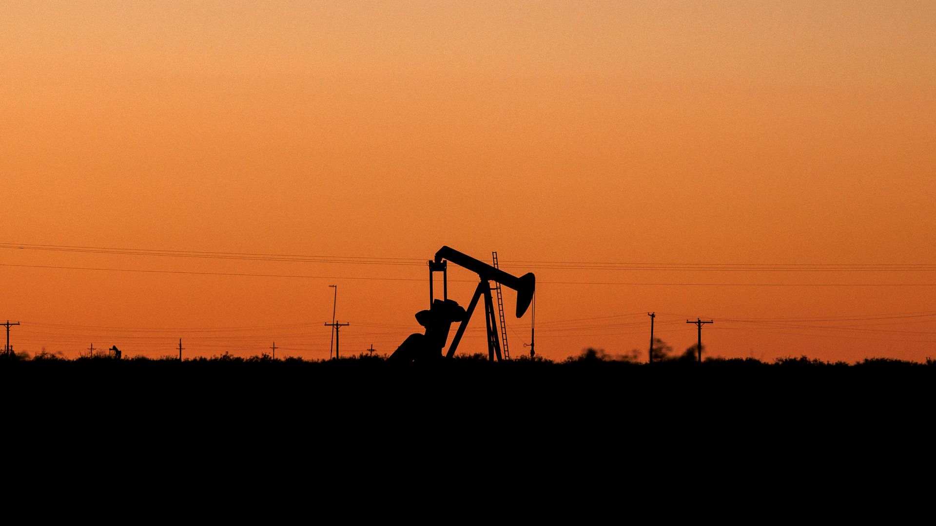 Silhouette of an oil pumpjack with power lines along the horizon at sunset; orange sky fades to purple, with a dark foreground.