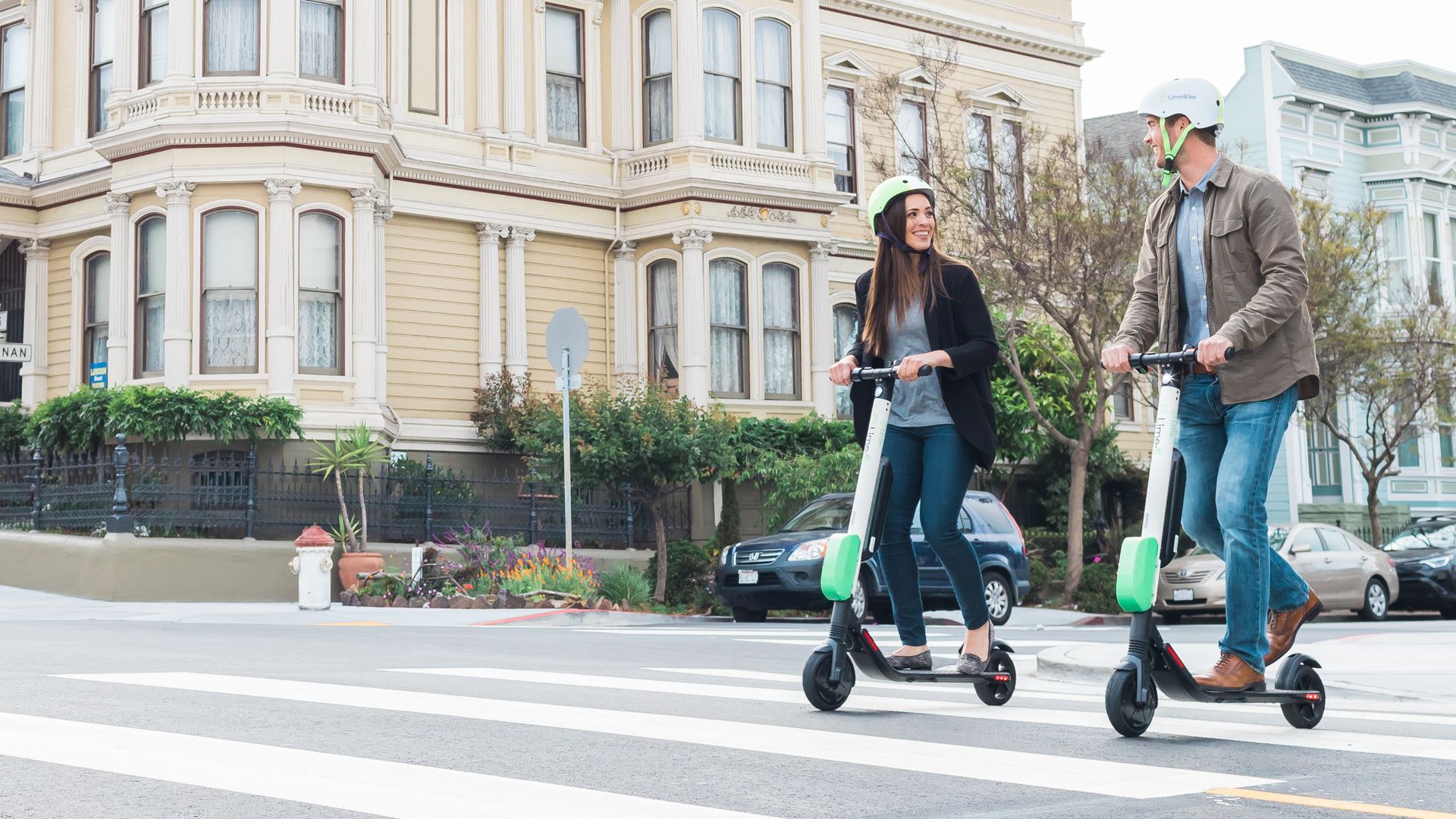 Photo of two riders on Lime scooters in a city. 