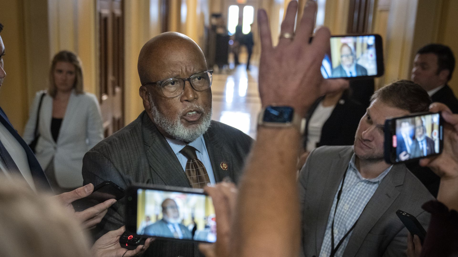 Rep. Bennie Thompson wearing a gray suit, blue shirt and brown tie, speaks with reporters at the Capitol as some film him on their phones.