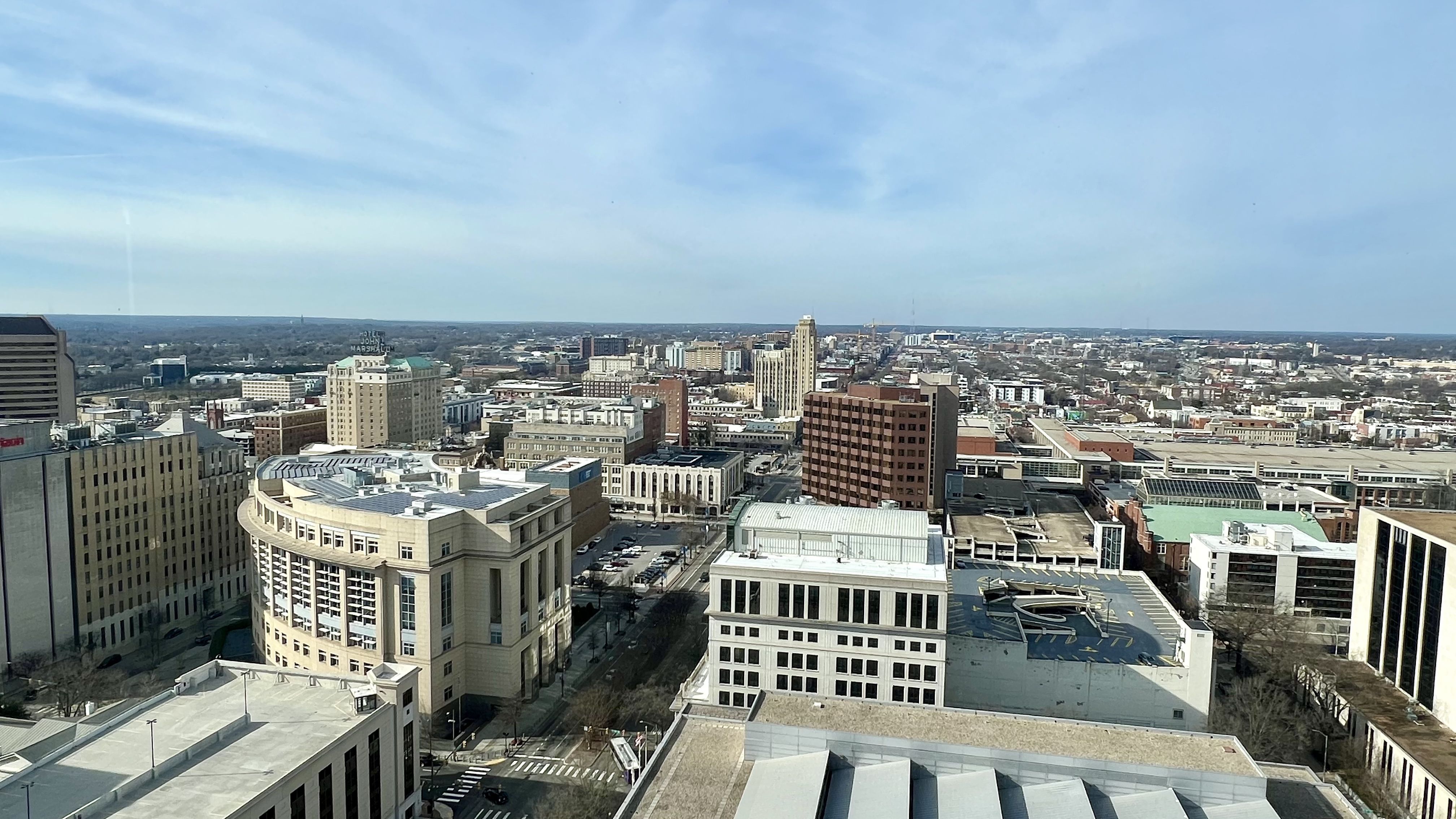 Cityscape with various buildings including a curved beige building, a brown high-rise, and a hotel with a rooftop sign. Clear blue sky above and streets visible below.