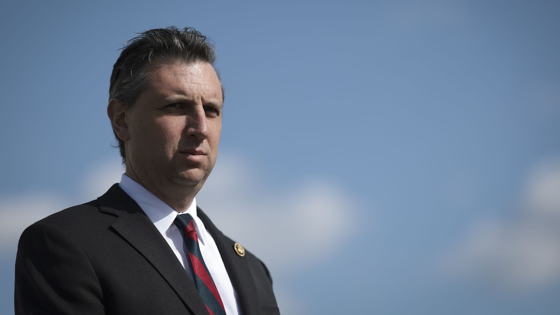 Rep. Seth Magaziner, wearing a dark gray suit and standing in front of a blue sky.