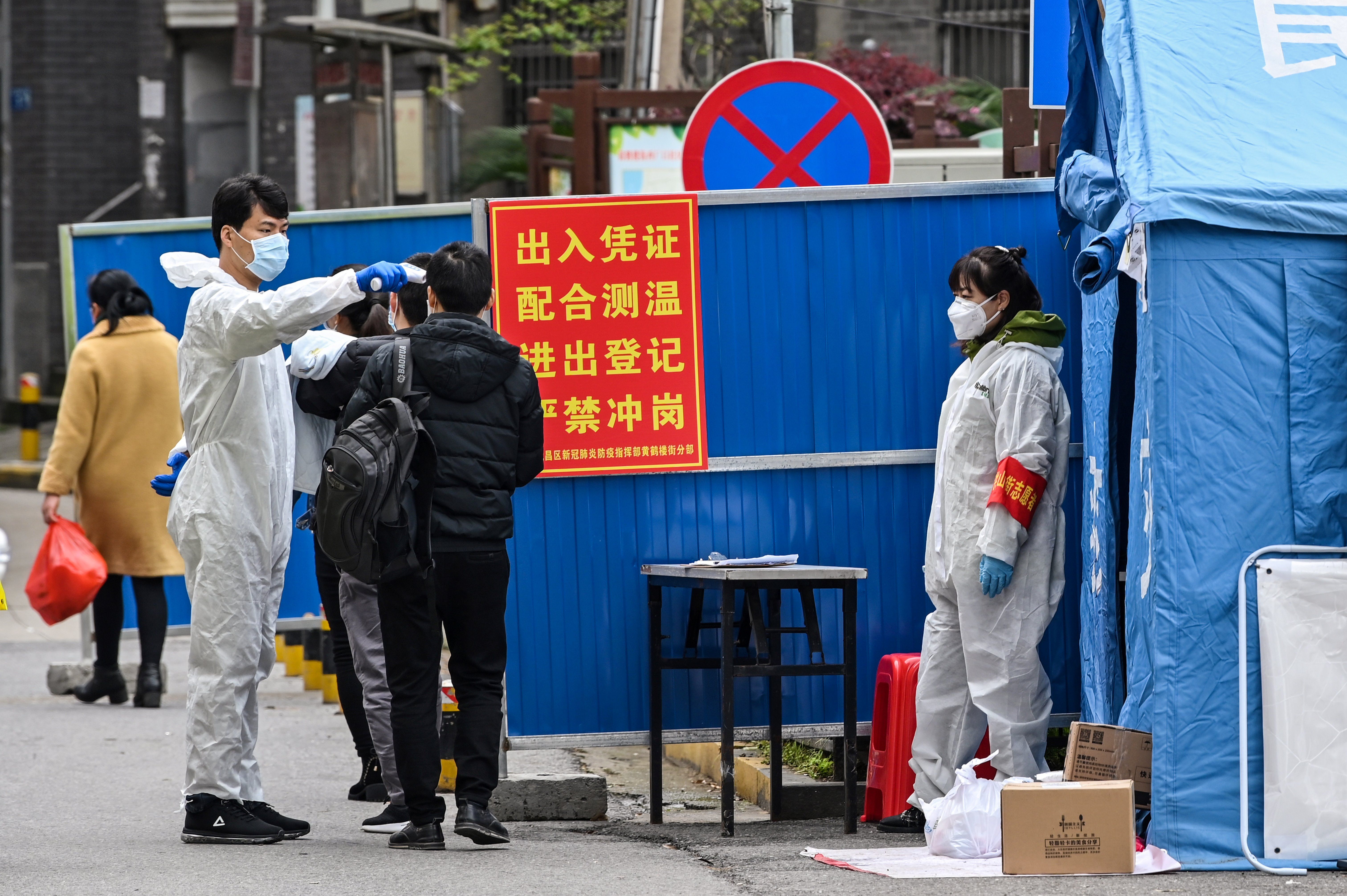 A man wearing a protective suit takes the temperature in a neighborhood in Wuhan, in China's central Hubei province on March 30, 2020