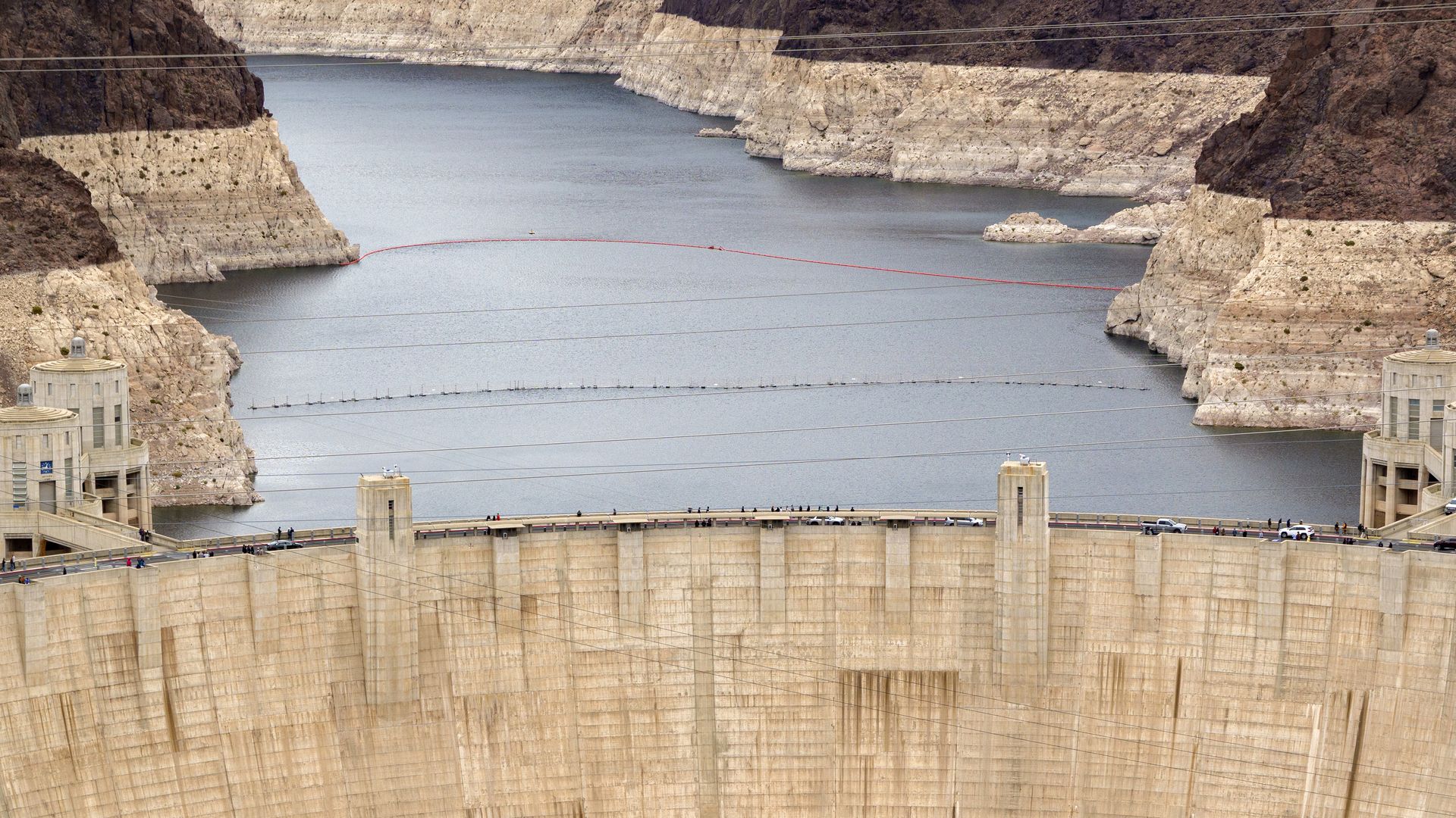 A huge concrete dam holds back a river, with white portions of the brown rock along the sides showing a long-term reduction of water levels. 