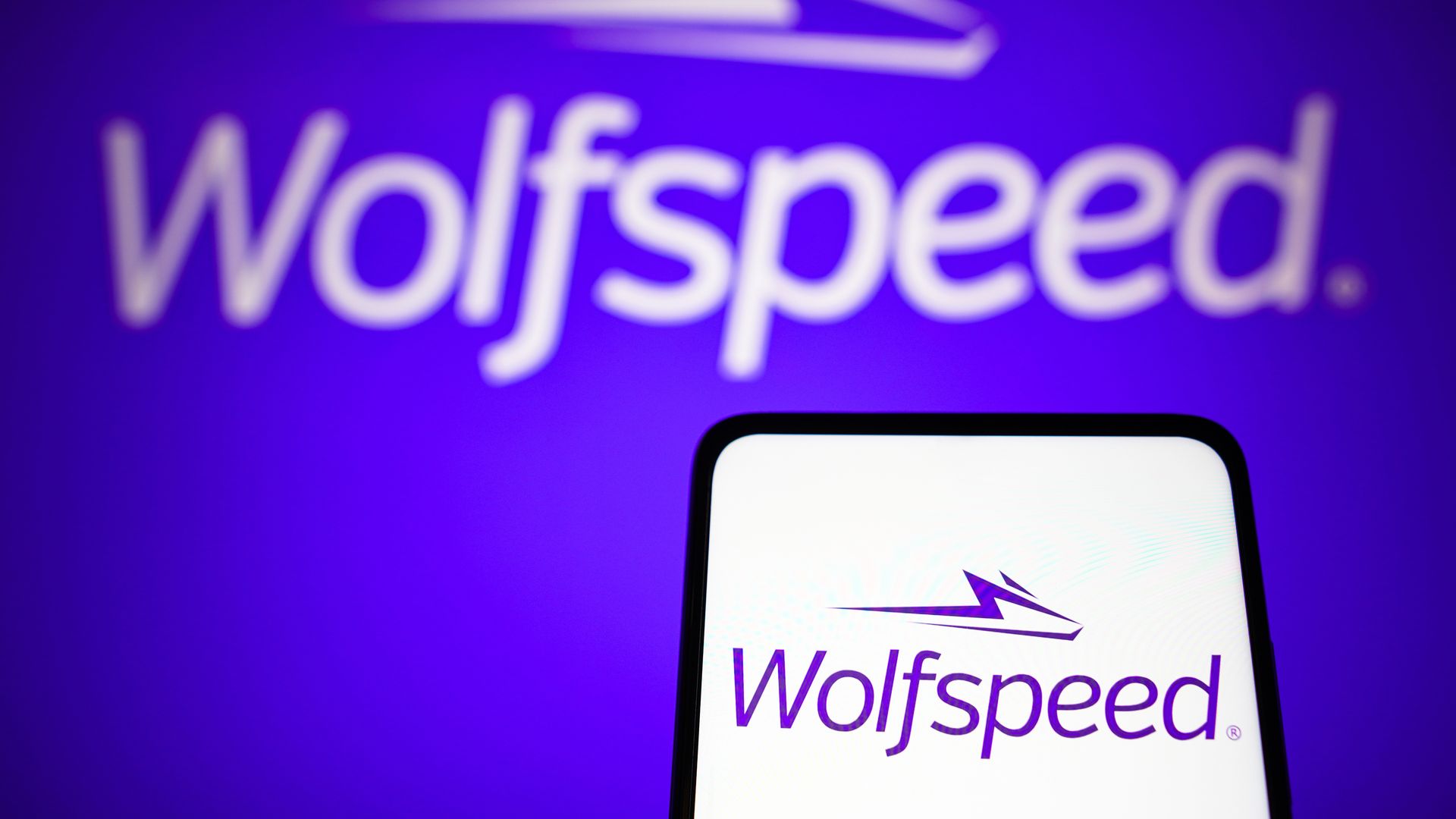 The Wolfspeed logo on a phone in front of a Wolfspeed logo on a wall. 